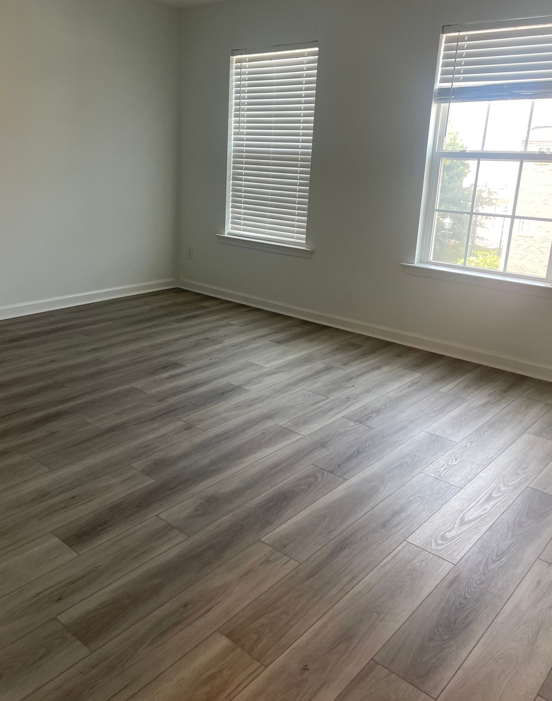 An empty room with hardwood floors and two windows.
