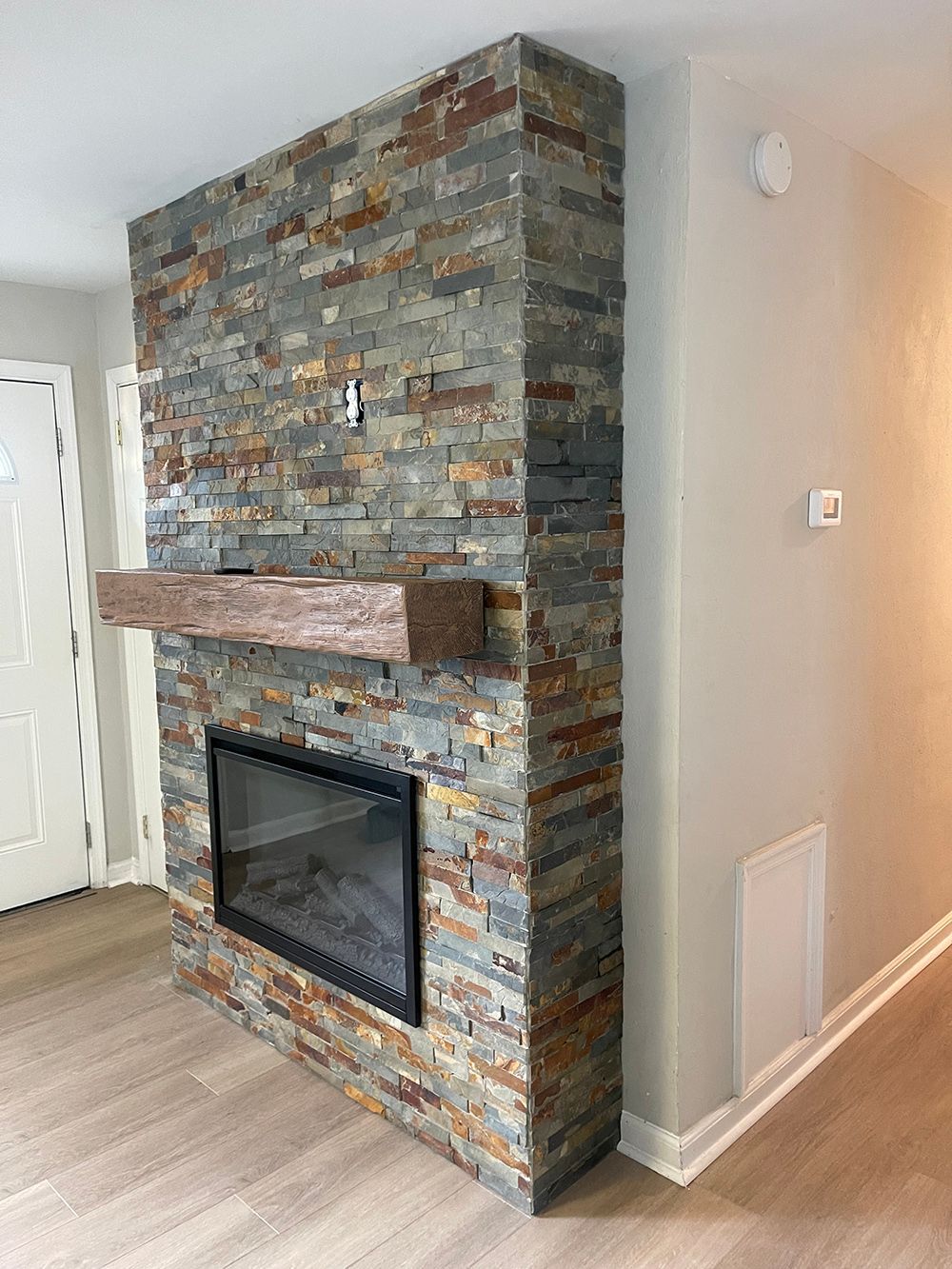 A fireplace with a stone wall and a wooden mantle in a living room.