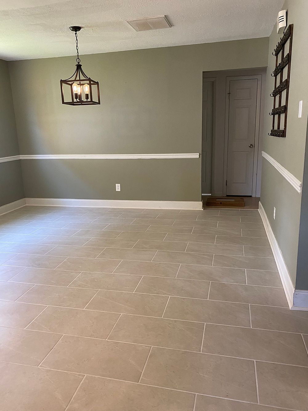 An empty dining room with tile floors and a chandelier hanging from the ceiling.