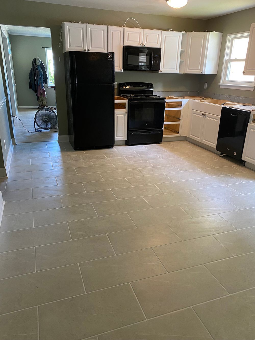 A kitchen with white cabinets , a black refrigerator , a stove , and a microwave.