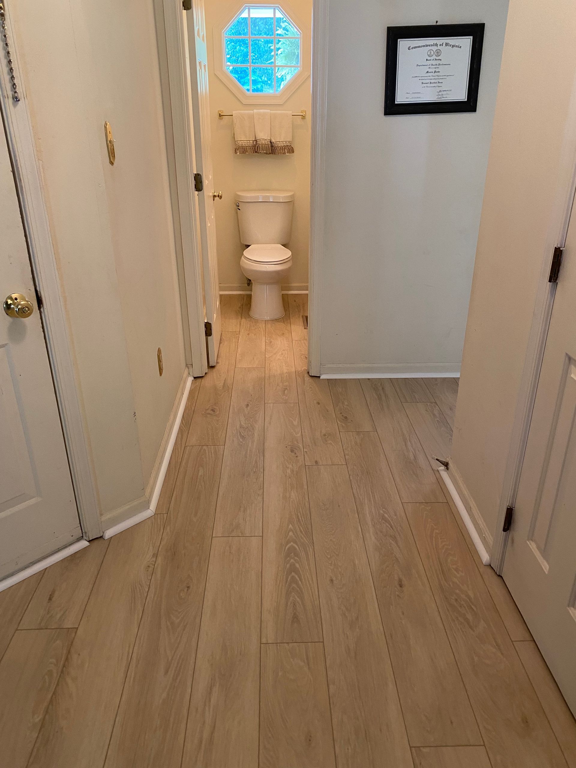 A hallway leading to a bathroom with a toilet and a window.
