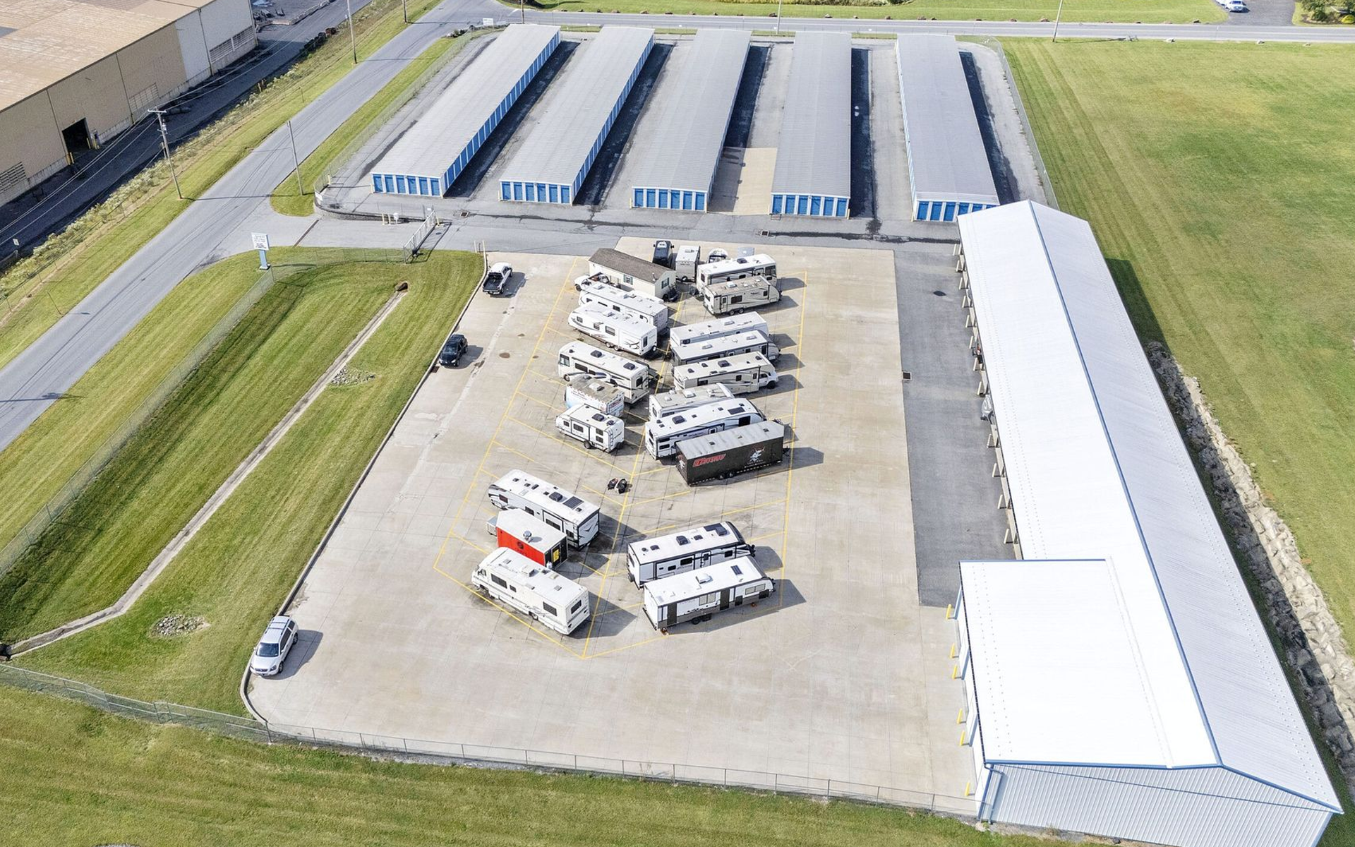 Aerial view of storage units and parked RVs. Blue-roofed storage units, light gray parking area.