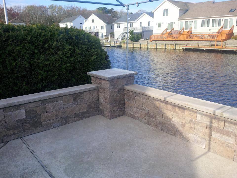 A brick wall overlooking a body of water with houses in the background