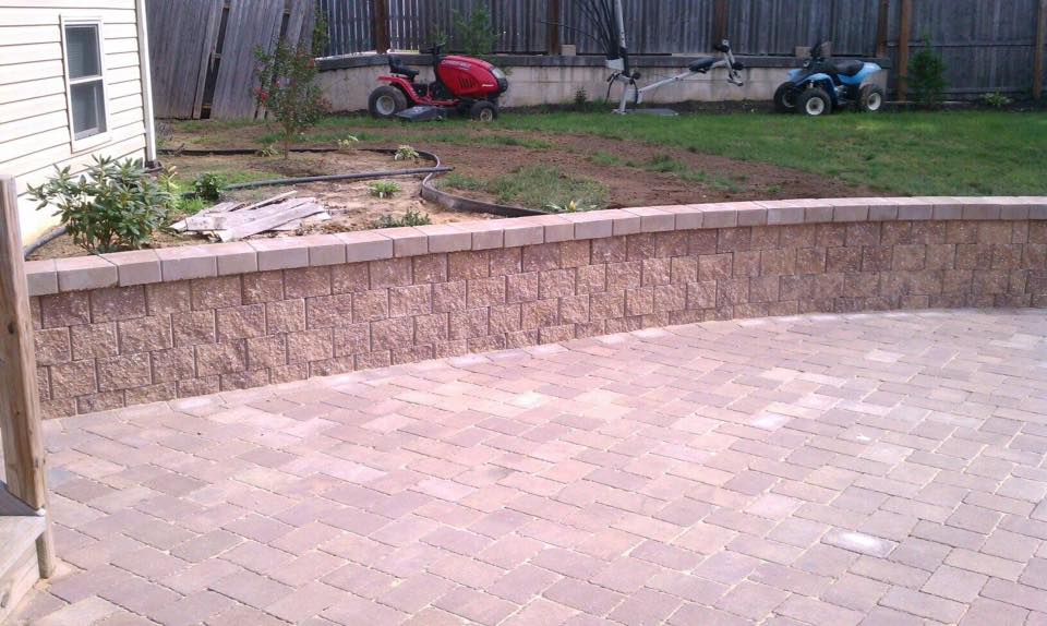 A lawn mower is parked in a backyard next to a brick wall.