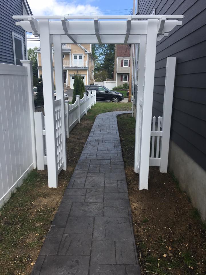 A walkway leading to a house with a pergola and a white fence.