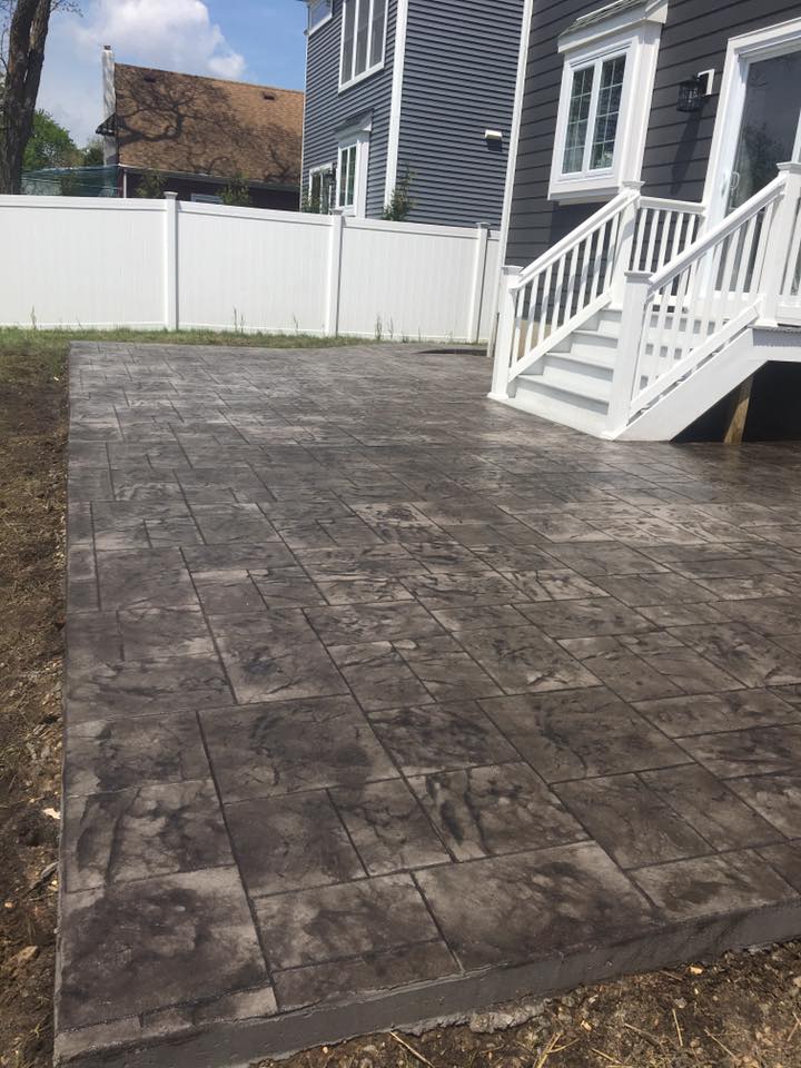 A patio with a deck and stairs in front of a house.