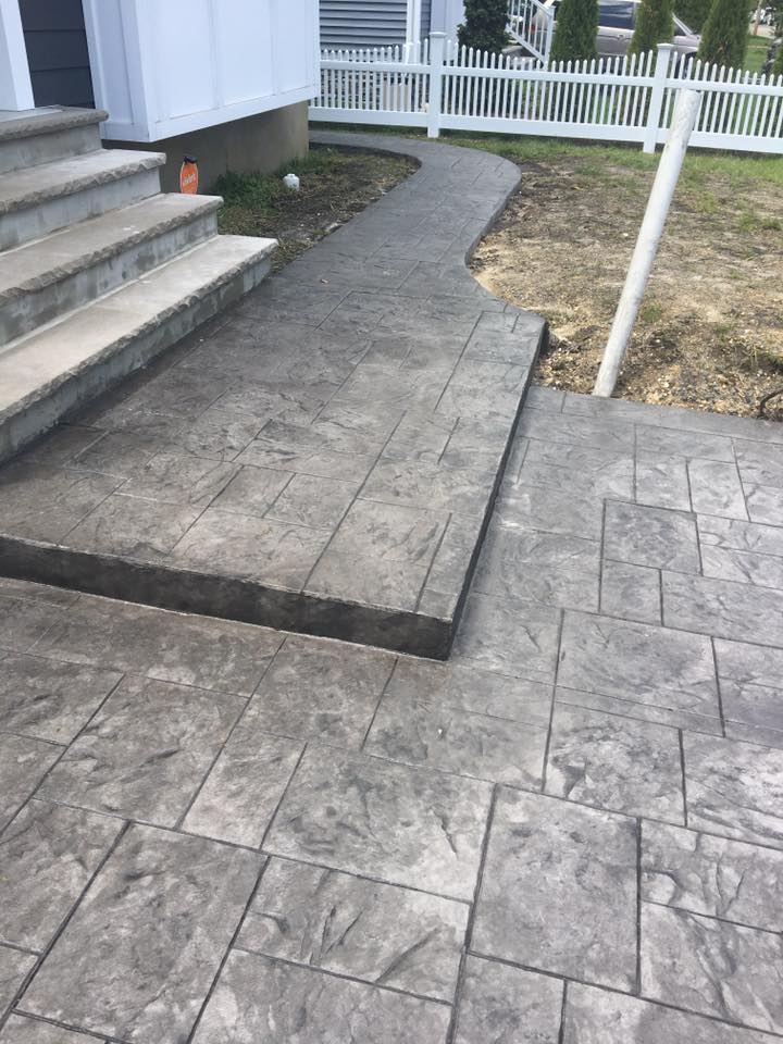 A concrete walkway with stairs and a white fence in the background.