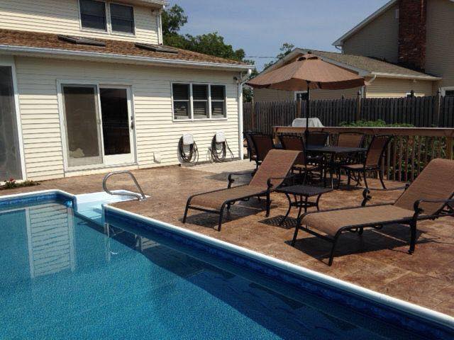 A swimming pool with chairs and umbrellas in front of a house.