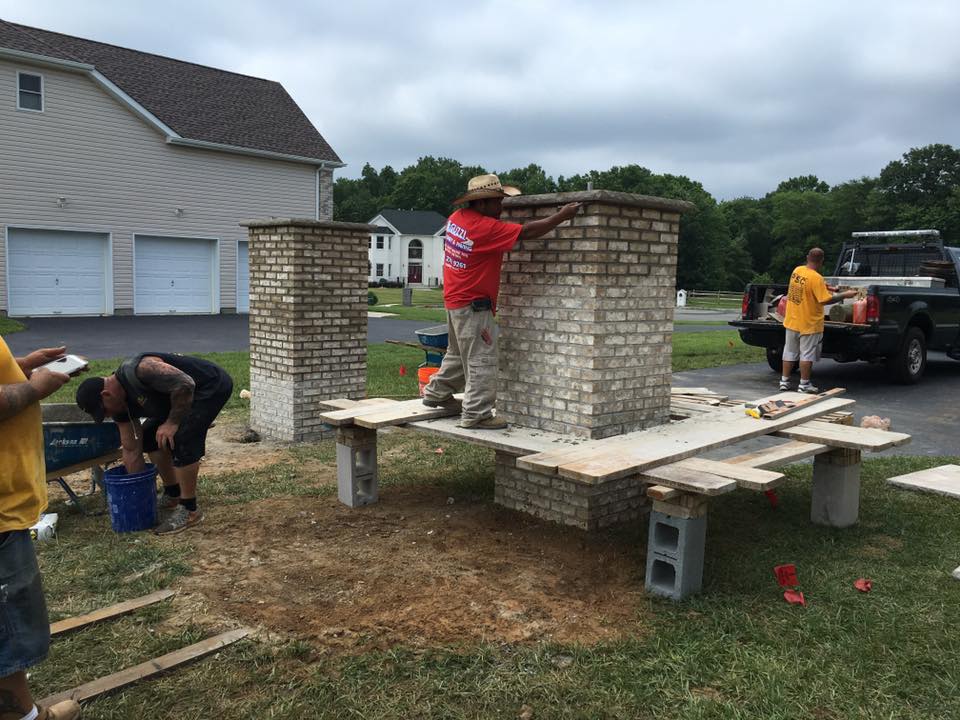 A group of people are working on a brick chimney in a yard.