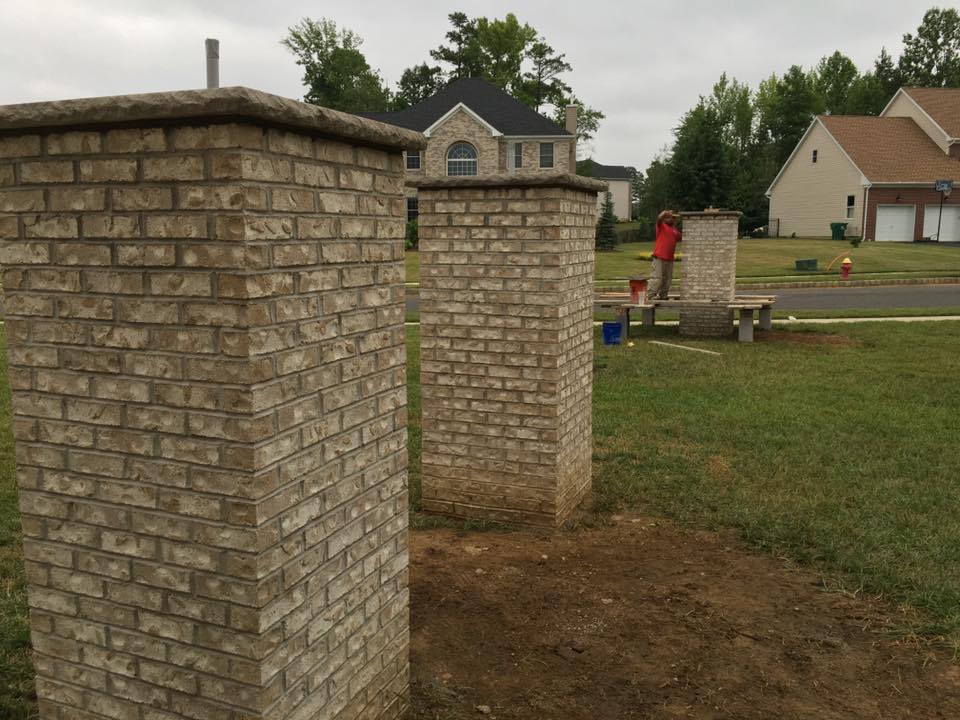A couple of brick pillars in a field with a house in the background