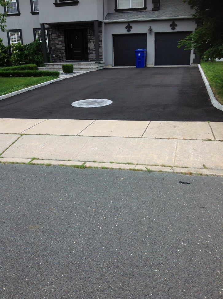 A driveway with a blue trash can in front of a house