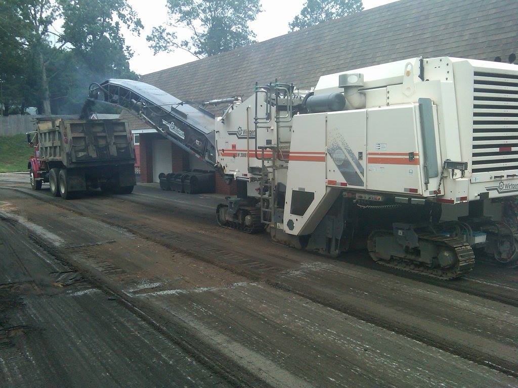 A large machine is working on a road next to a dump truck