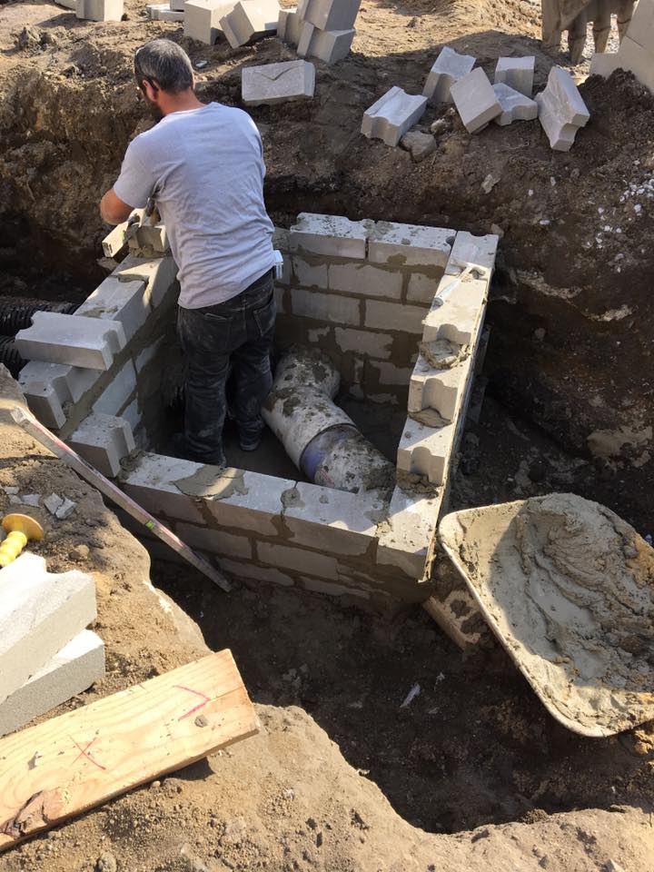 A man is working on a brick wall with a pipe in it.