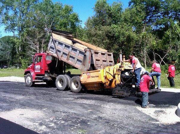 A dump truck is being loaded with asphalt in a parking lot.