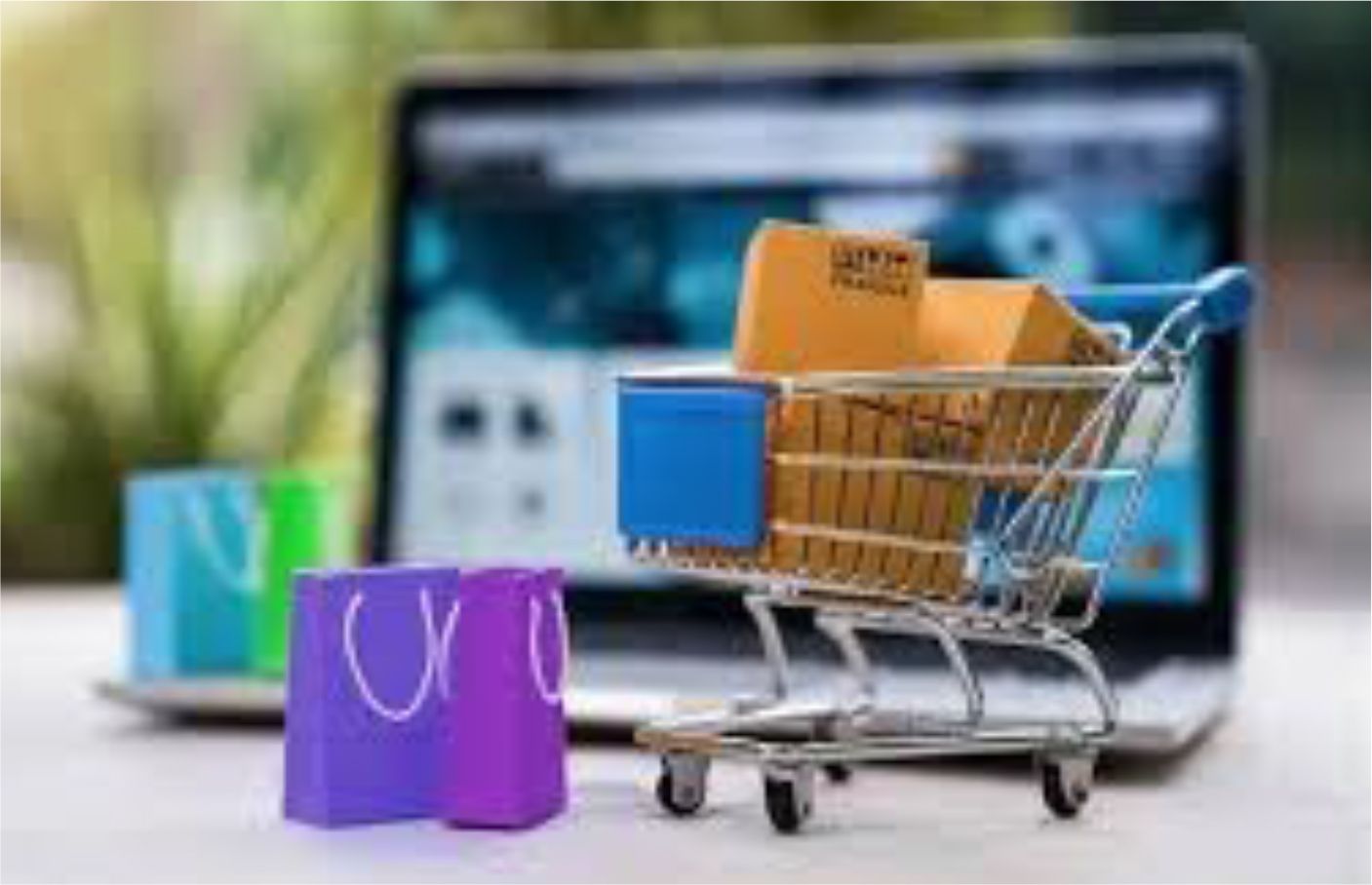 Shopping cart with boxes in front of laptop showing a website with shopping bags nearby.