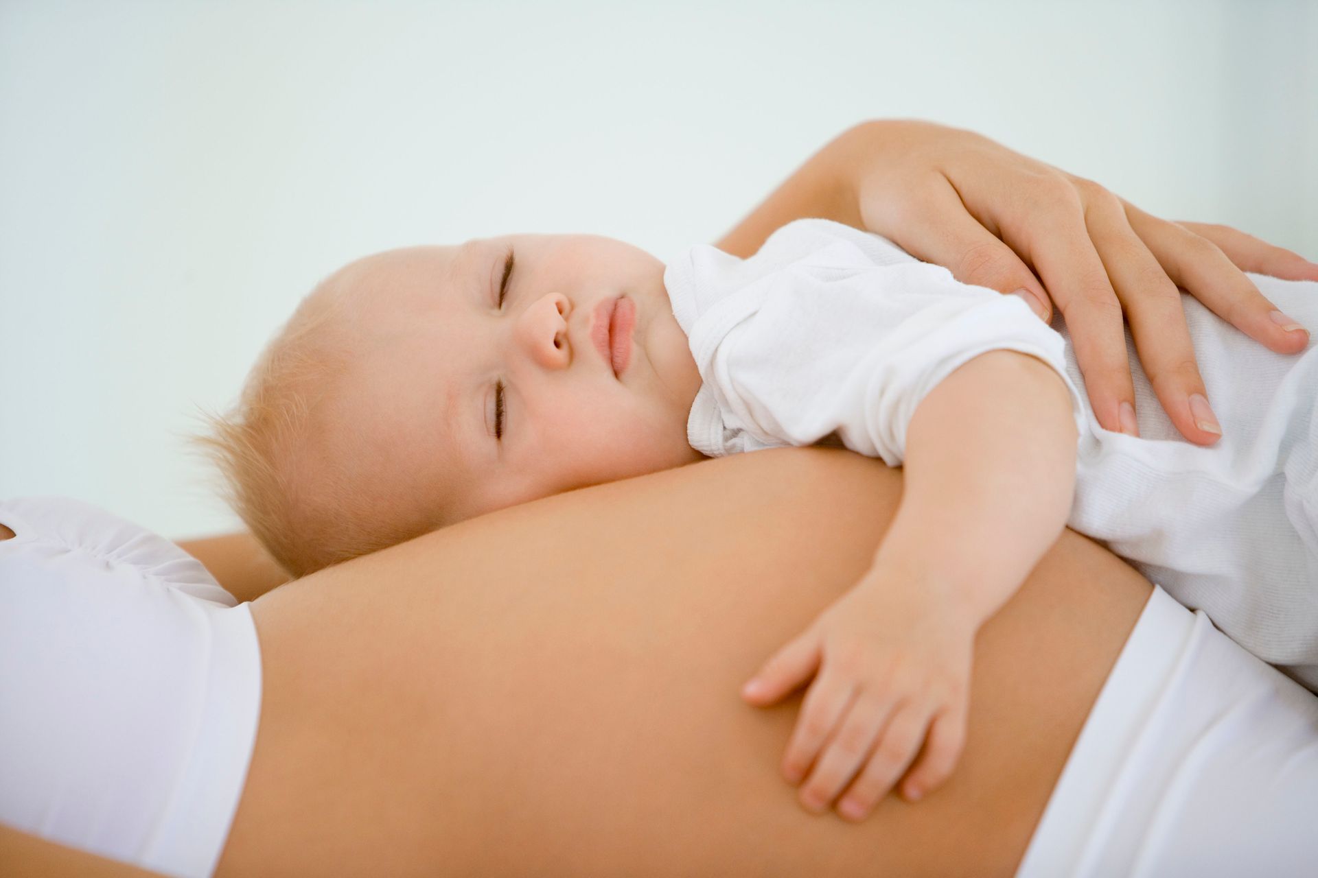 Baby sleeping on a pregnant person's belly, hand gently supporting the child.
