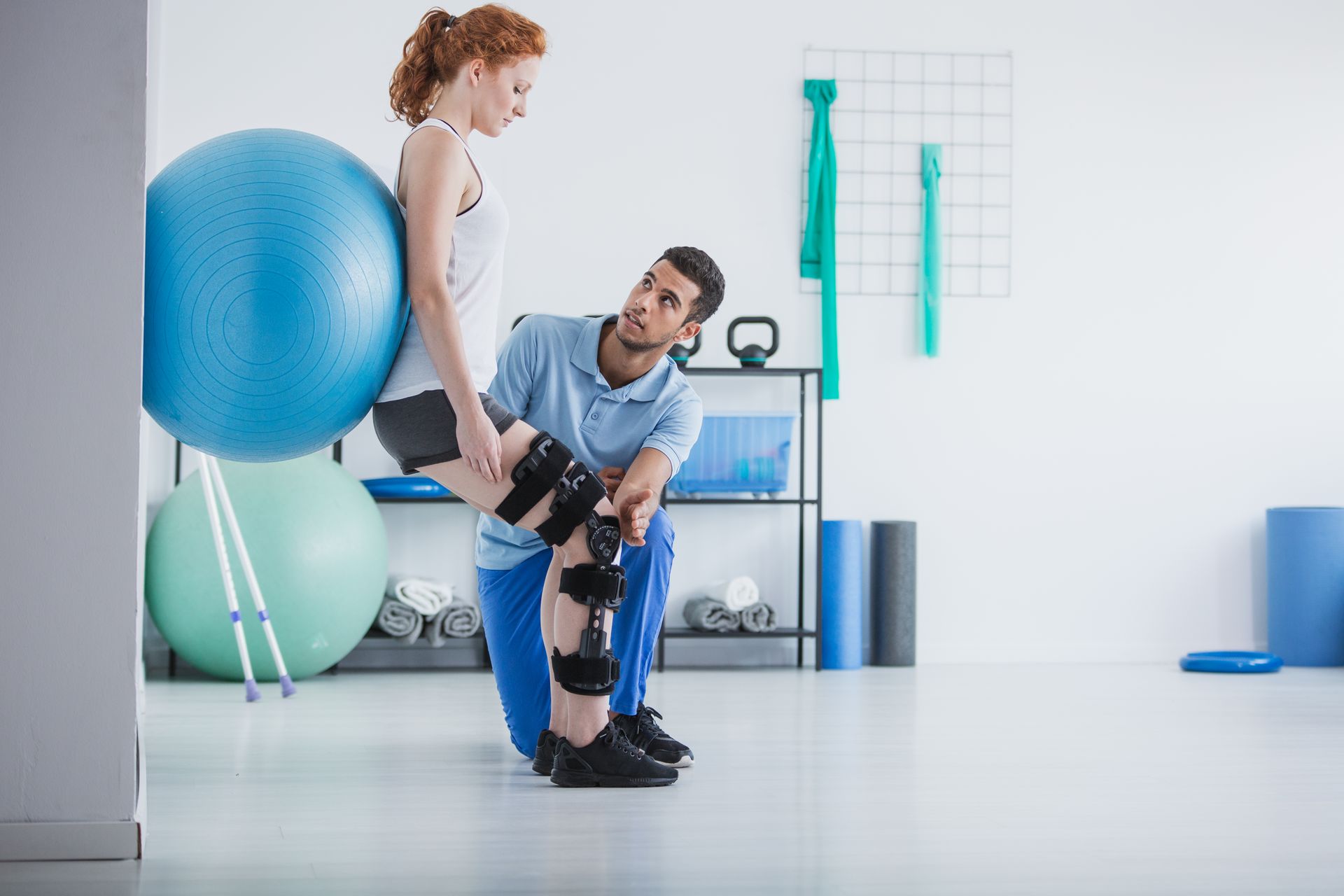 A man is helping a woman with a knee brace in a gym.