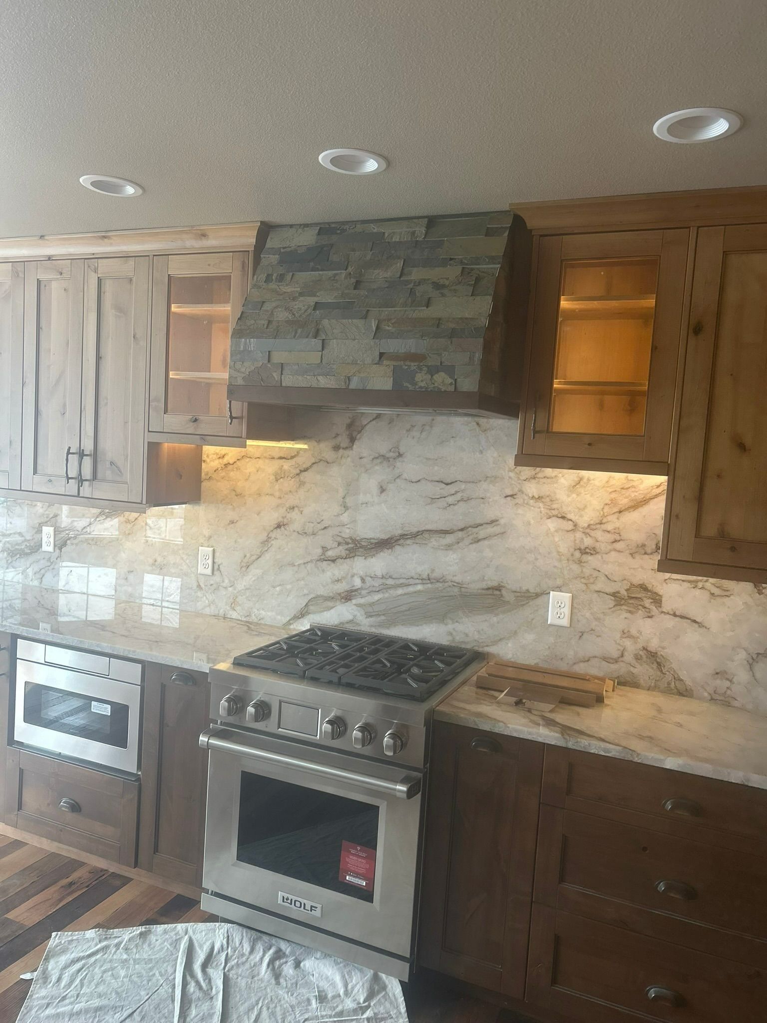 Kitchen with stainless steel appliances, stone range hood, light granite countertops, and wooden cabinets.