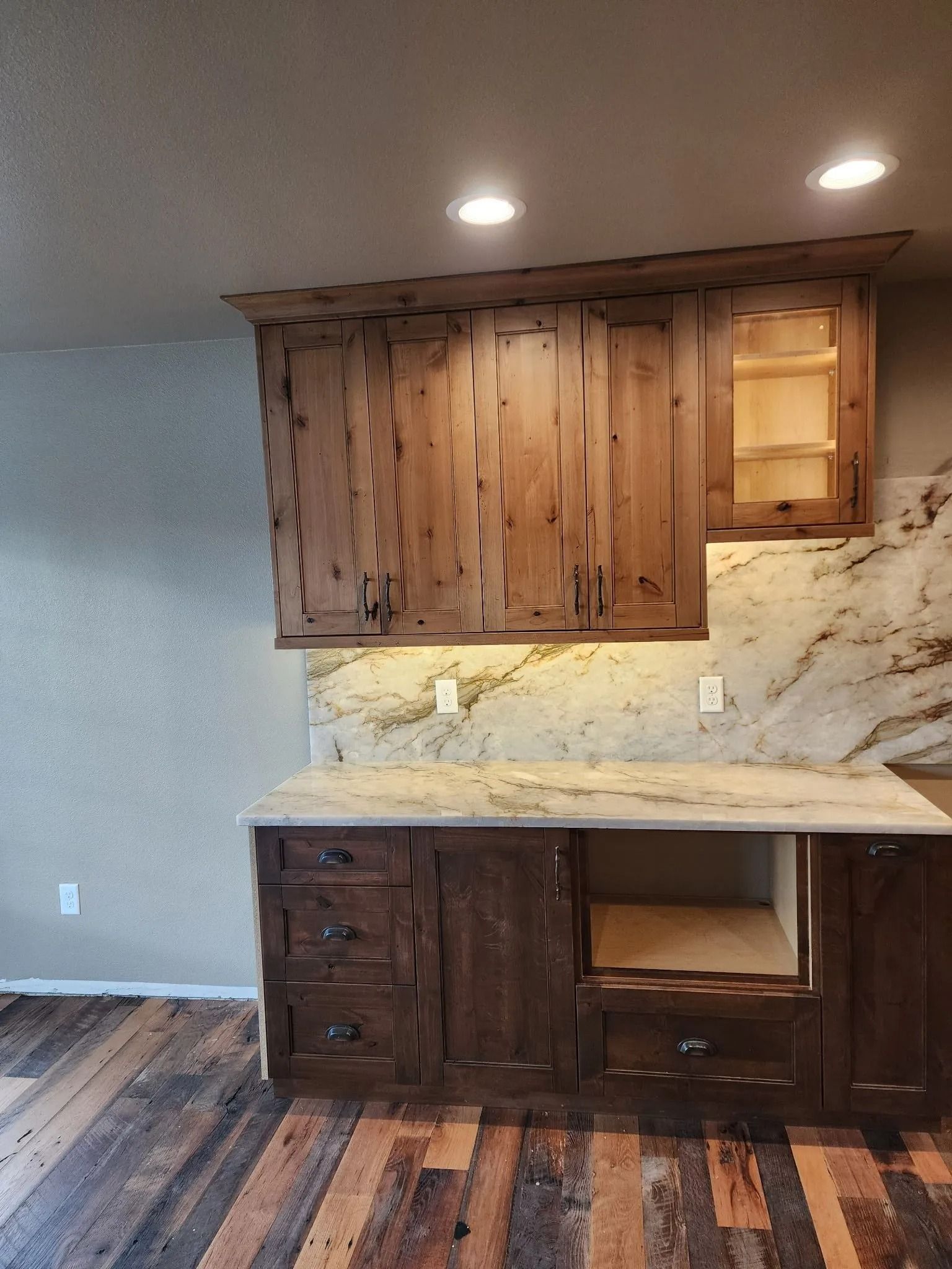 Rustic wooden kitchen cabinets with granite countertops and exposed wood floor.