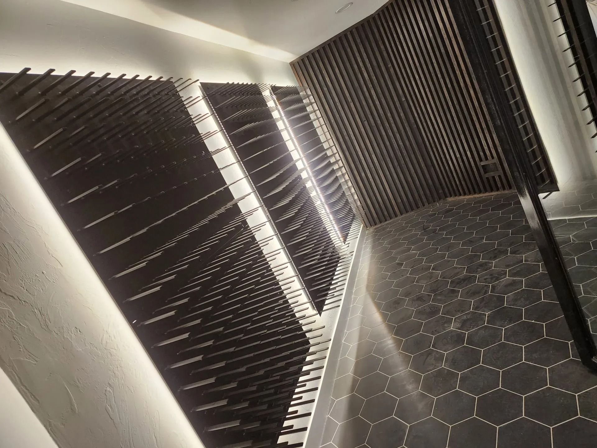 Staircase with hexagonal tile floor, dark wooden slats on the walls, and inset lighting.