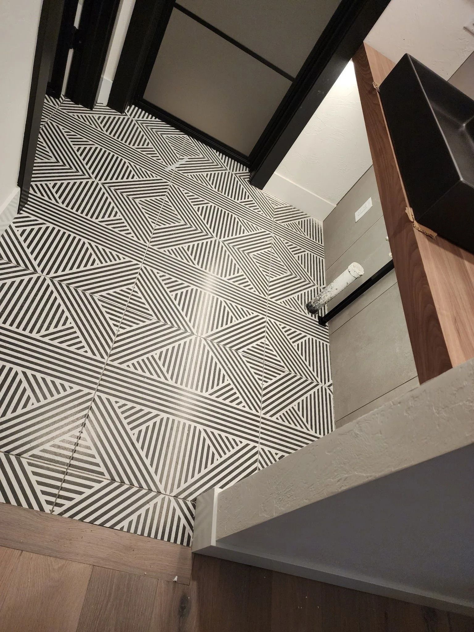 Black and white geometric tiled floor. Part of a room with a wooden counter and black beams.