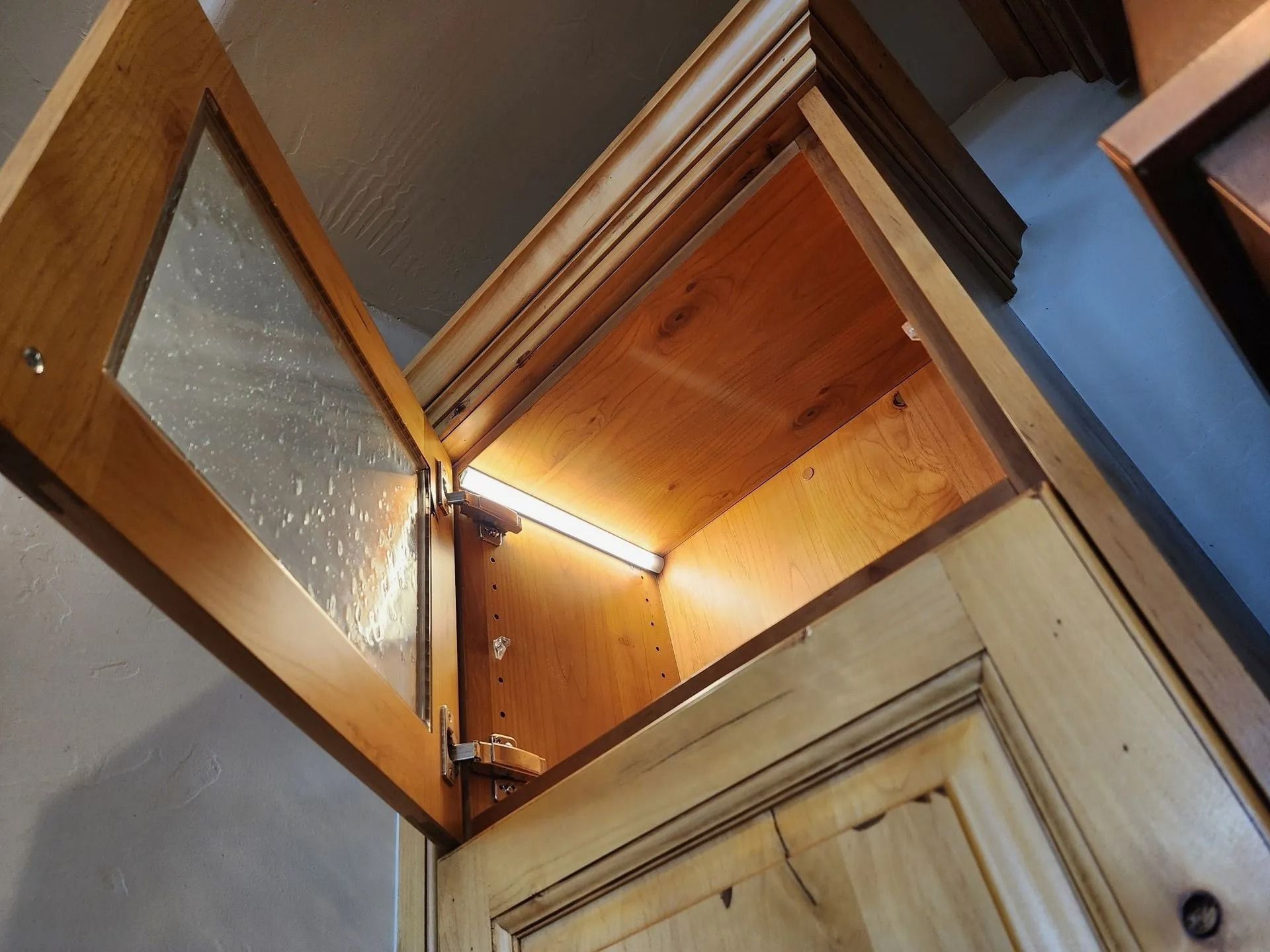 Open kitchen cabinet with glass door; interior illuminated by a light.