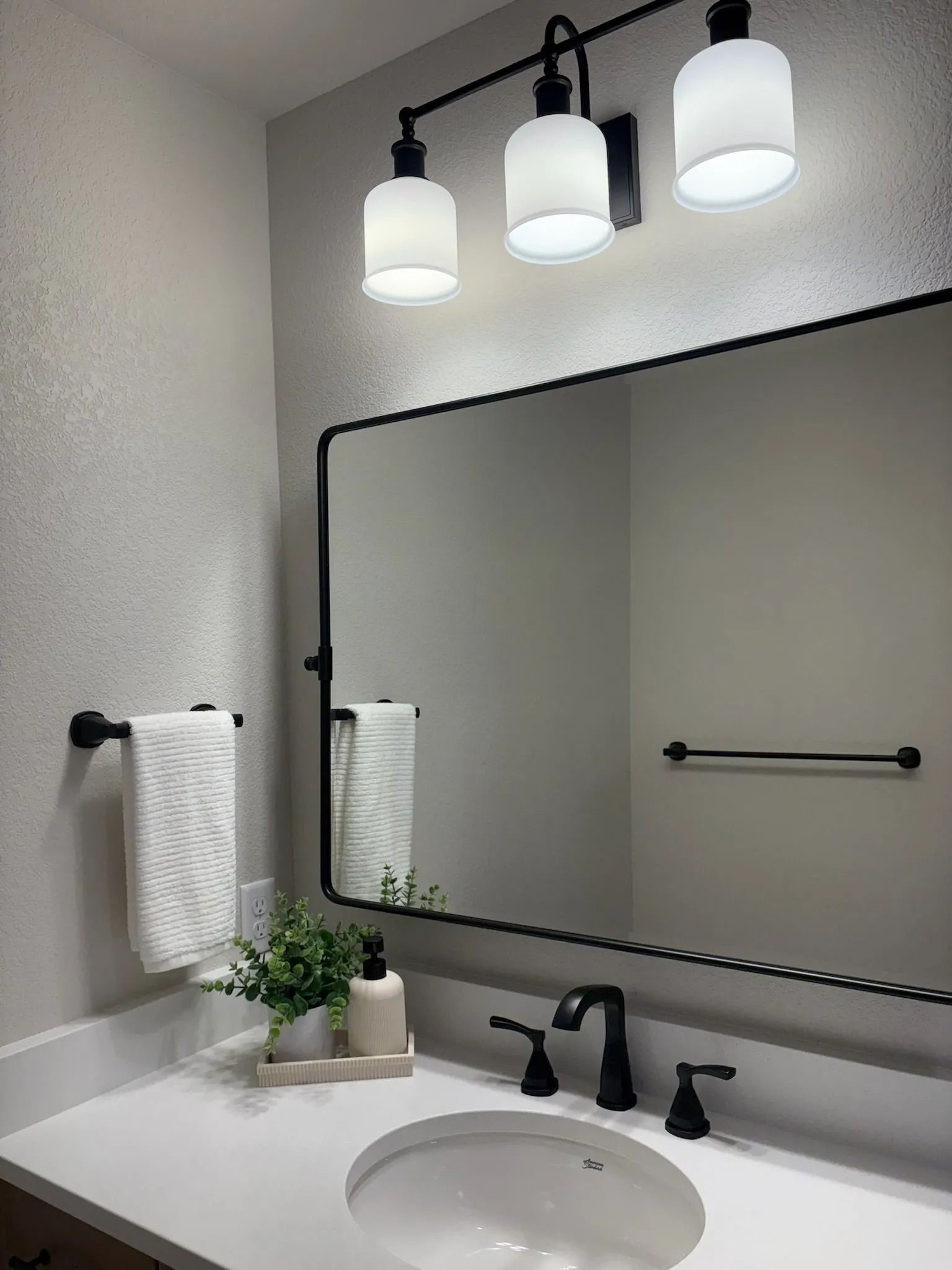 Bathroom with white countertop, black fixtures, and a large mirror with a black frame.