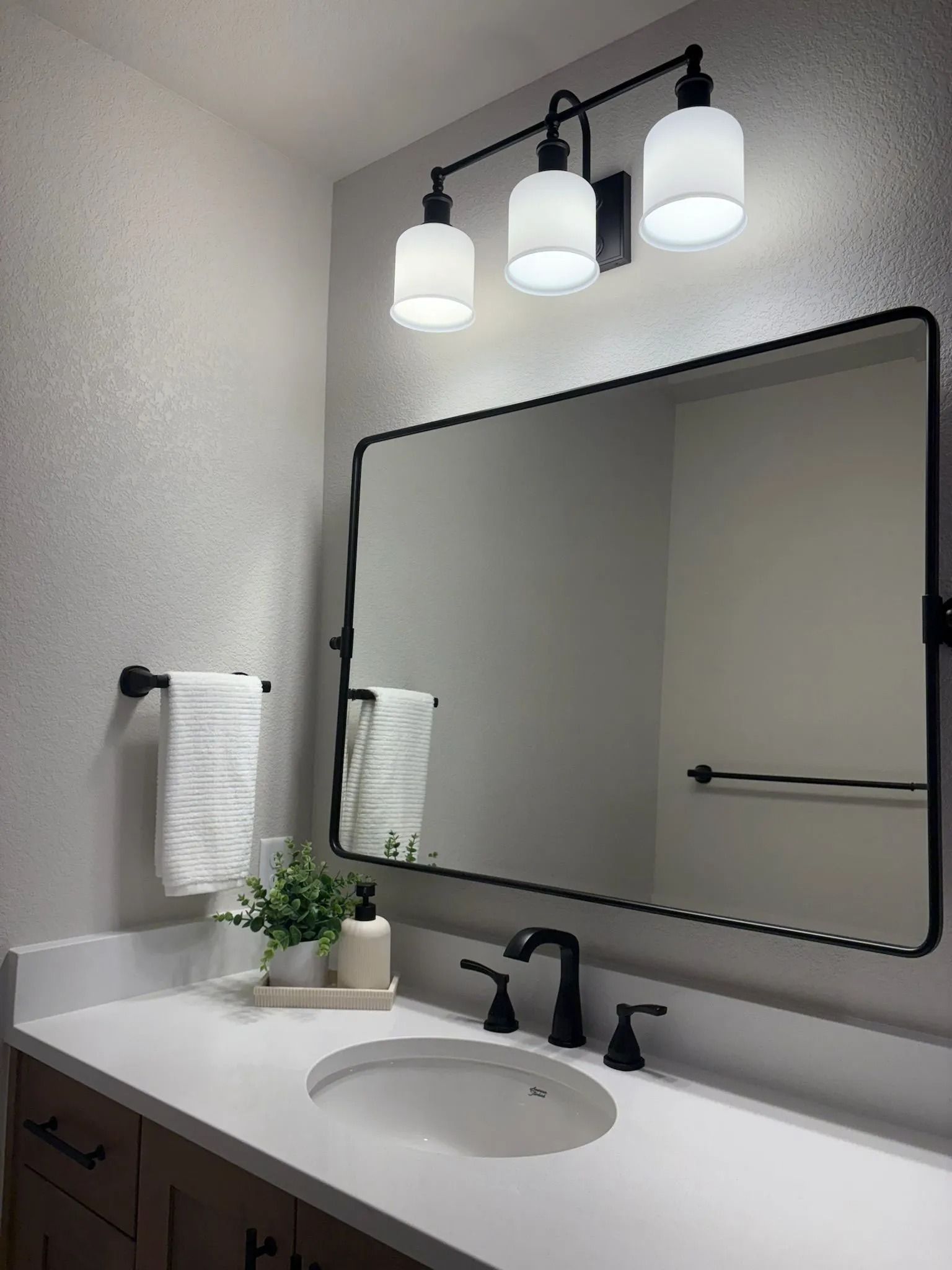 Bathroom with white countertop, black fixtures, mirror, and three-light vanity.