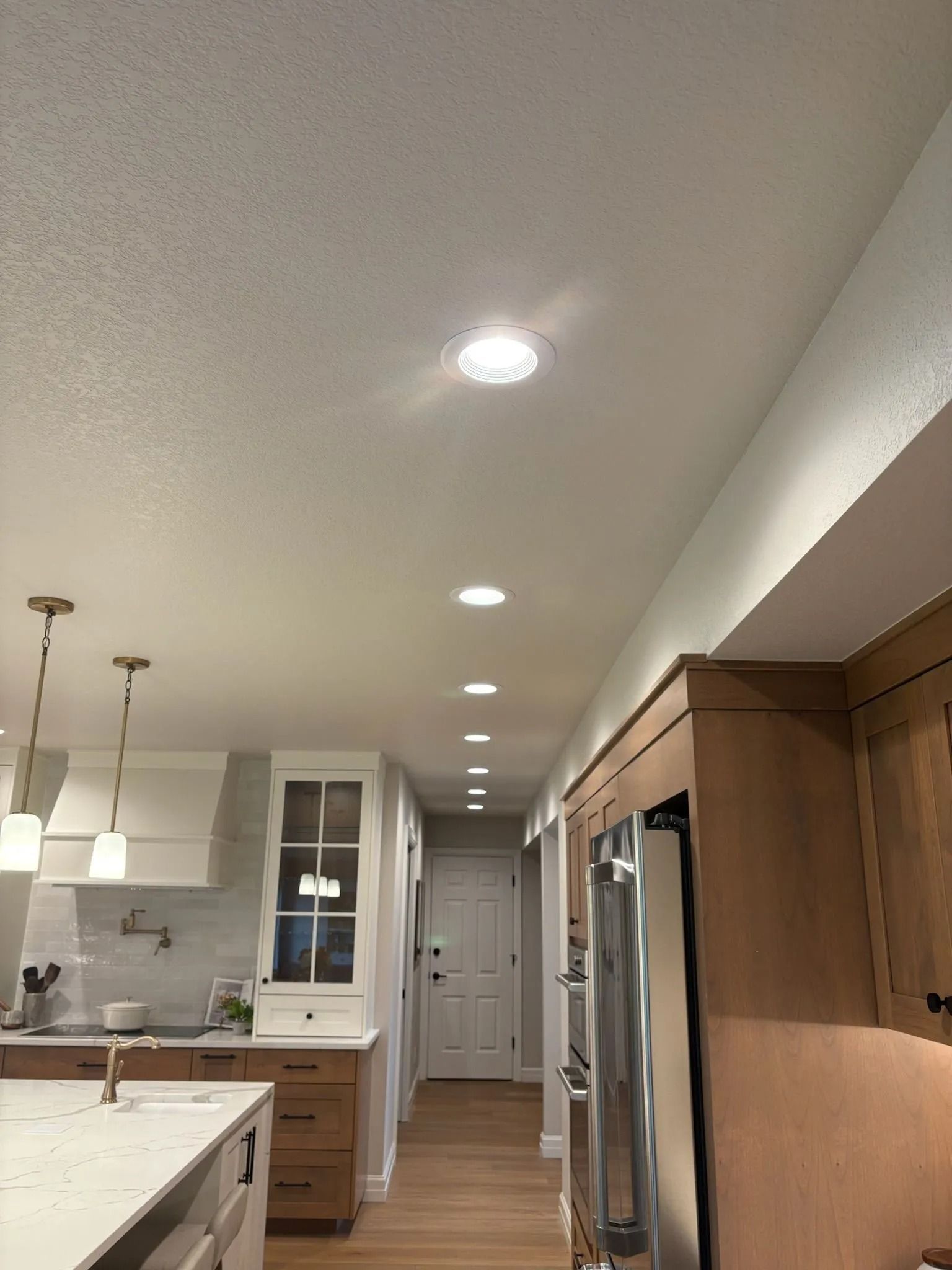 Kitchen with recessed lights in ceiling, wood cabinets, stainless steel appliances, and a hallway.