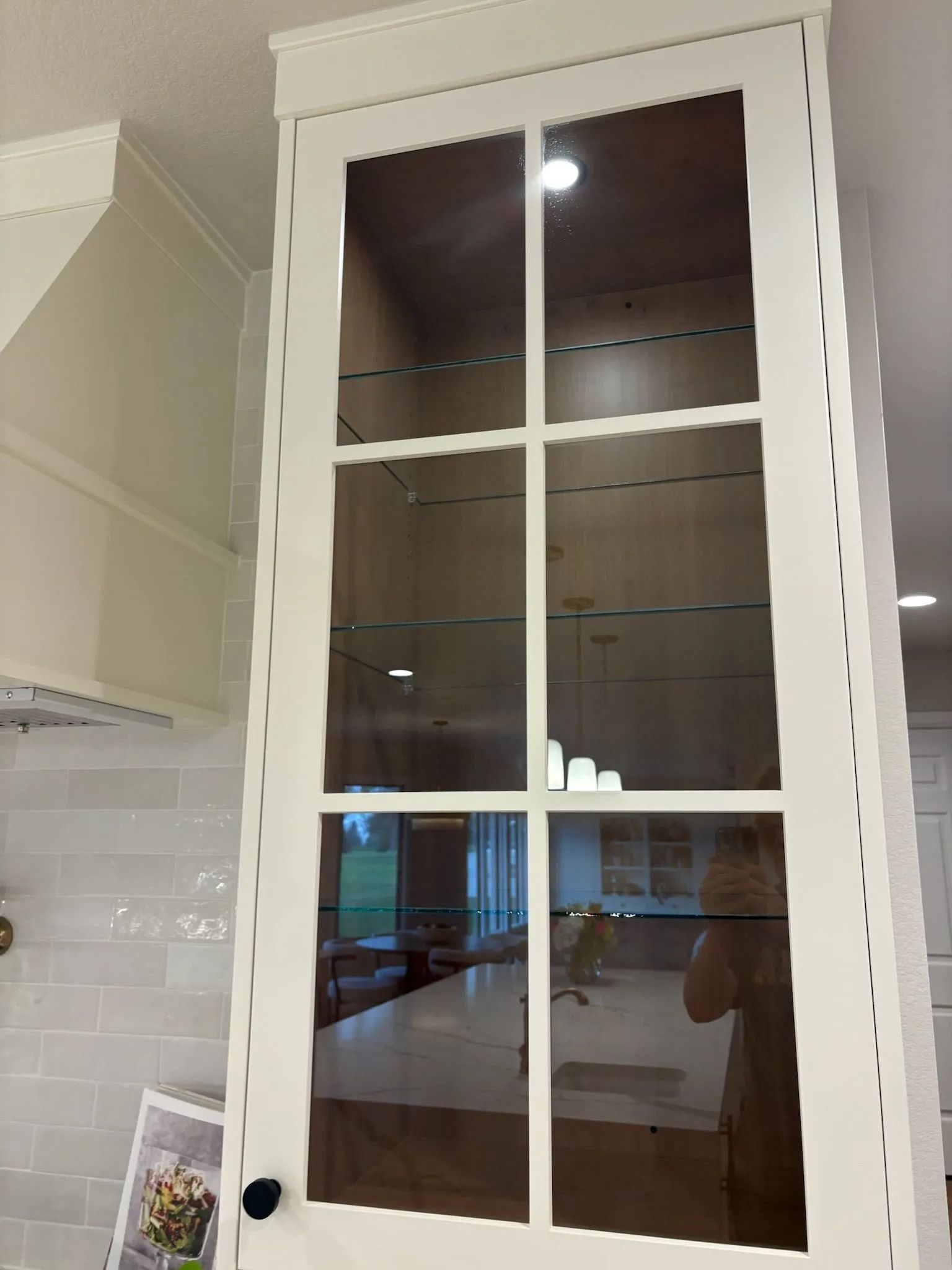 White kitchen cabinet with glass-paneled door. Interior shelves reflect surroundings.