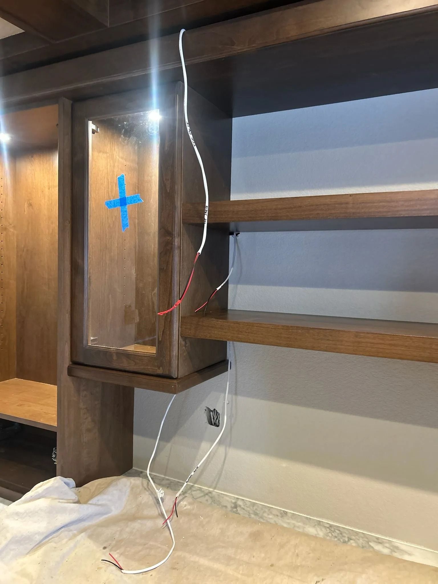 Wooden built-in shelving with exposed wiring running vertically and horizontally. Shelves are above a cabinet.