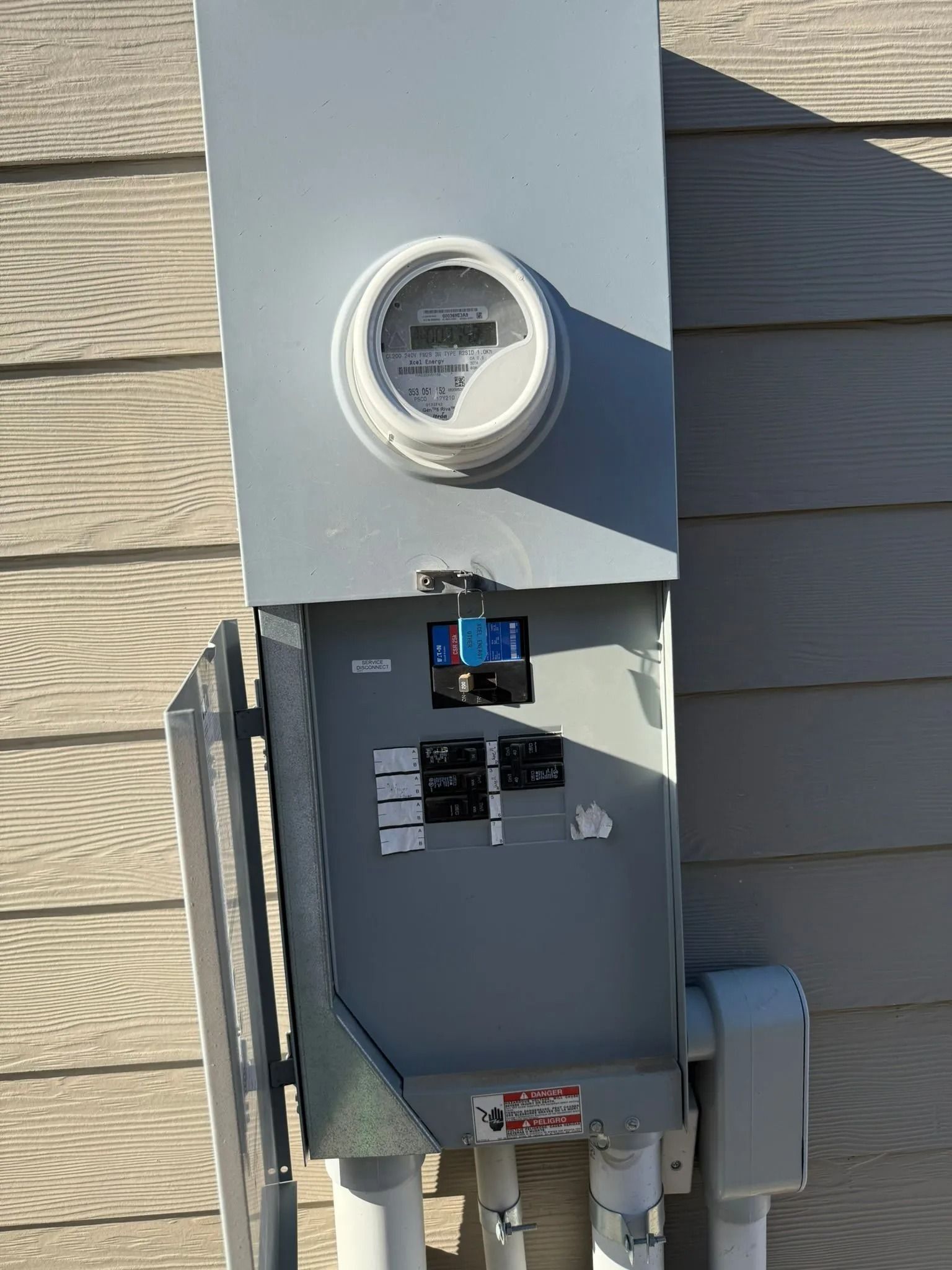 Electrical meter box on a building's exterior with meter, breakers, and conduits.