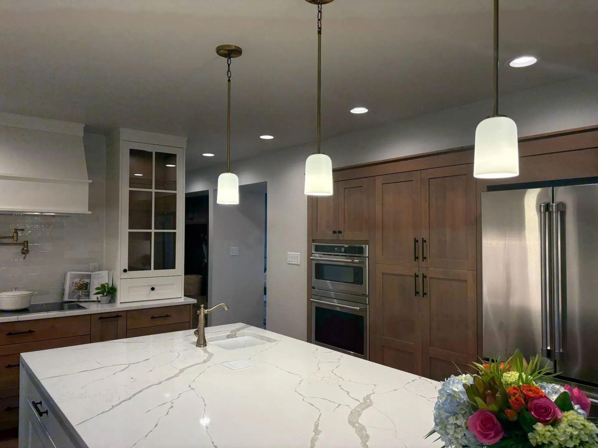 Kitchen with white countertop island, pendant lights, wooden cabinets, and stainless steel appliances.