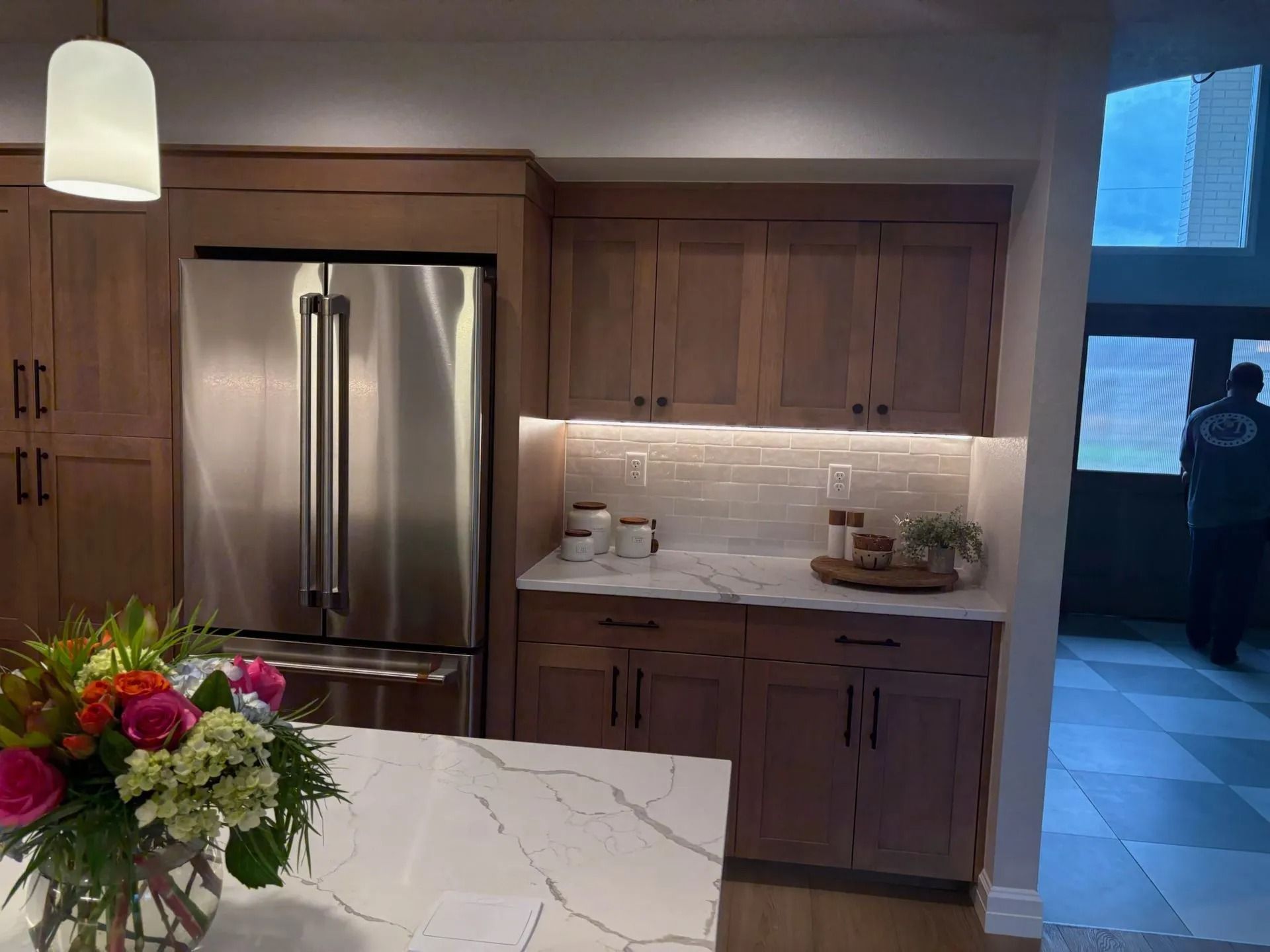 Modern kitchen with stainless steel refrigerator, wooden cabinets, and white countertop.