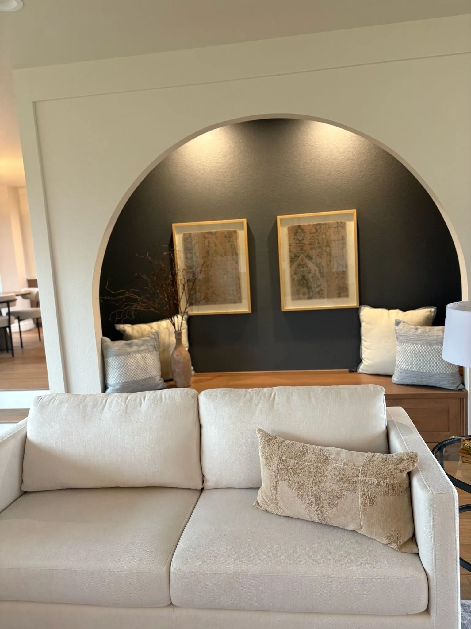 Cream-colored sofa in front of a curved alcove with art, pillows, and dark gray wall.