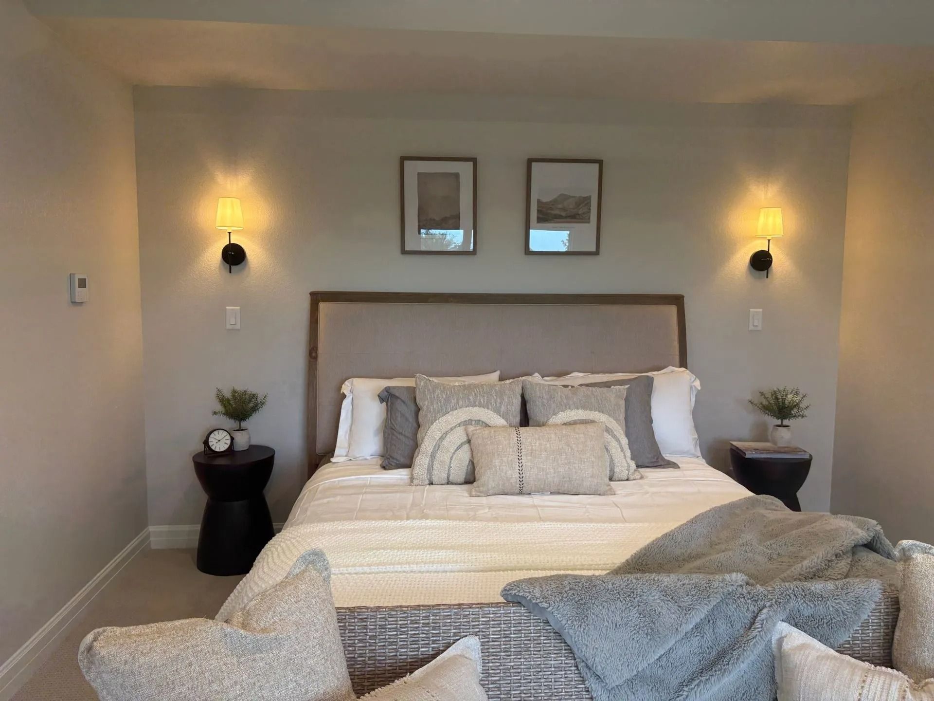 Bedroom with bed, neutral colors, artwork, sconces, and side tables.