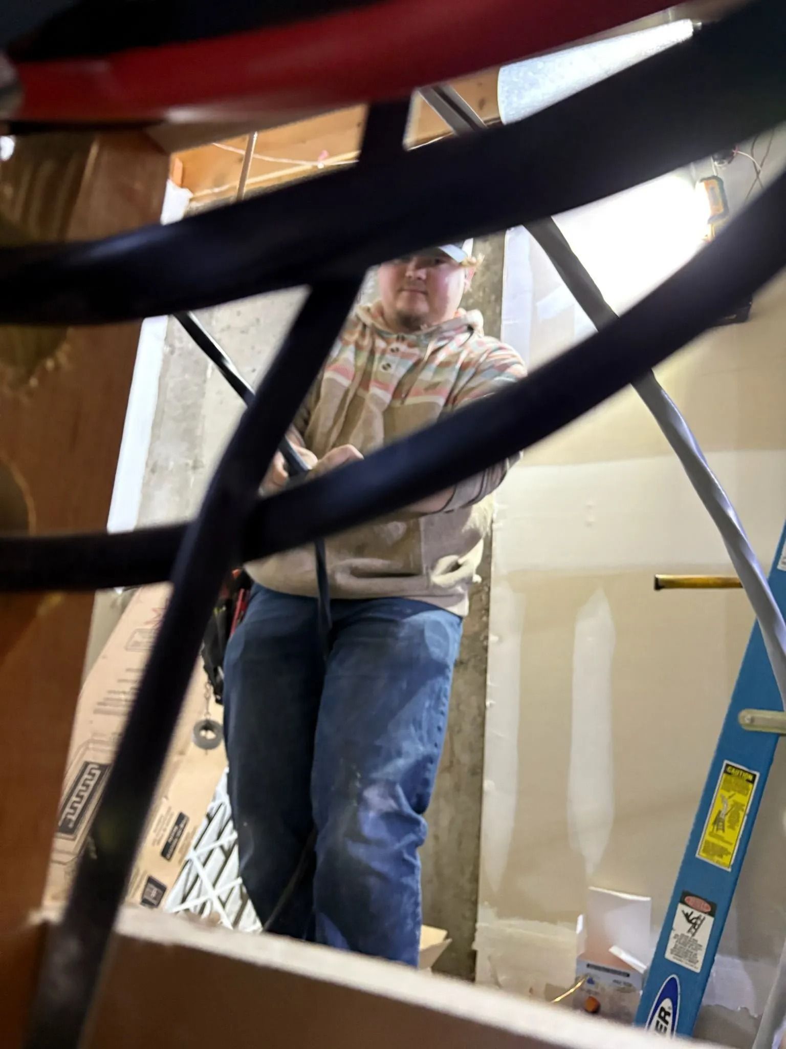 Person wearing a tan hoodie and blue jeans stands in a doorway, framed by black metal.