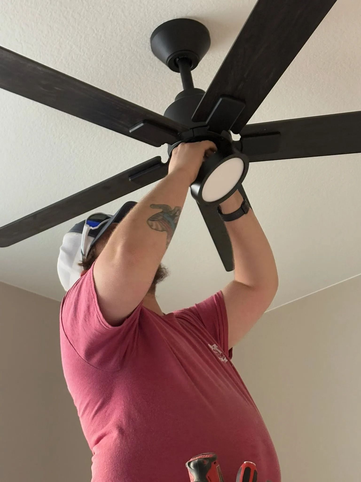 Person installing a black ceiling fan with lights in a room.