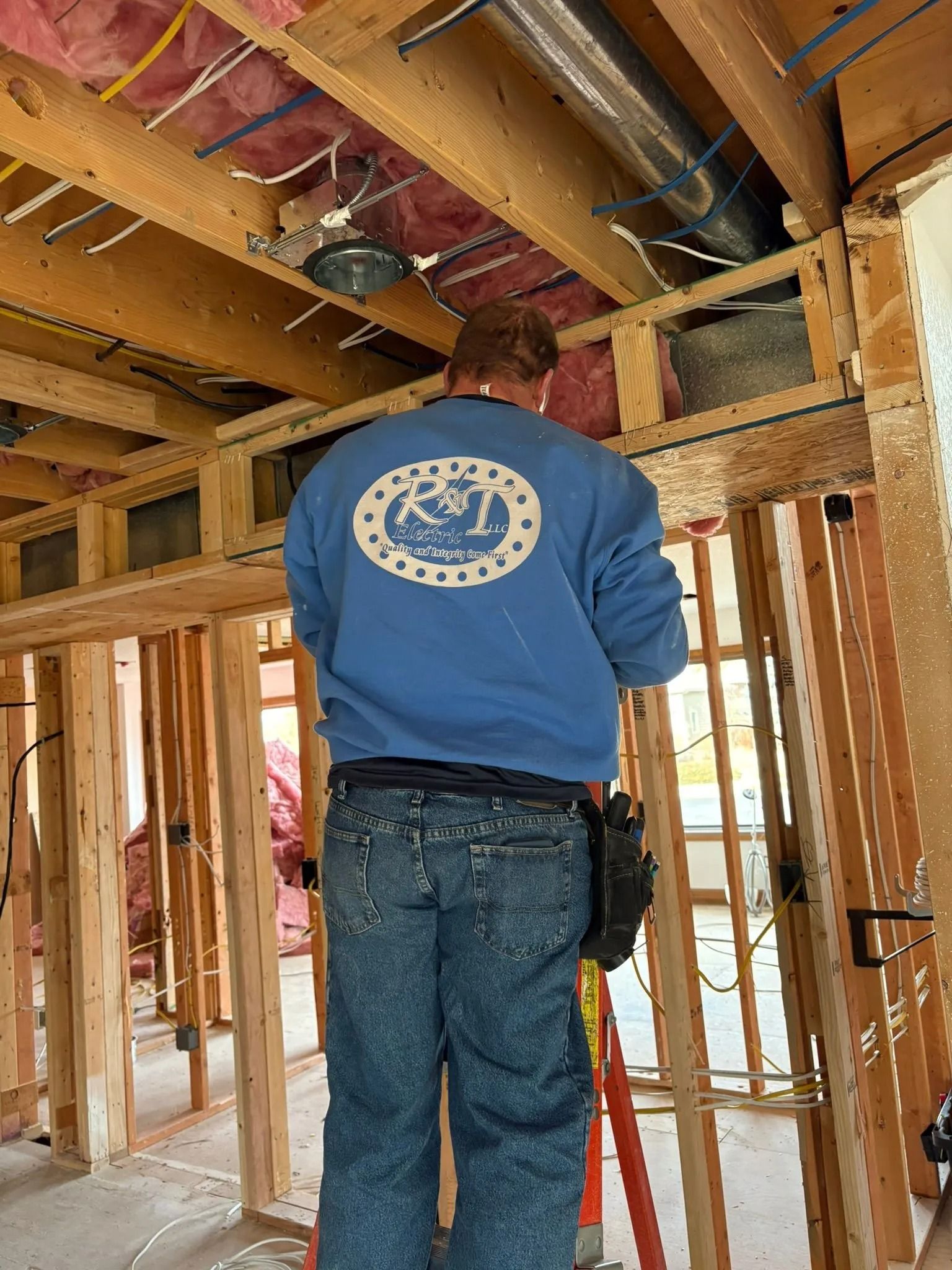Person in blue sweatshirt works on wiring in a wood-framed construction.