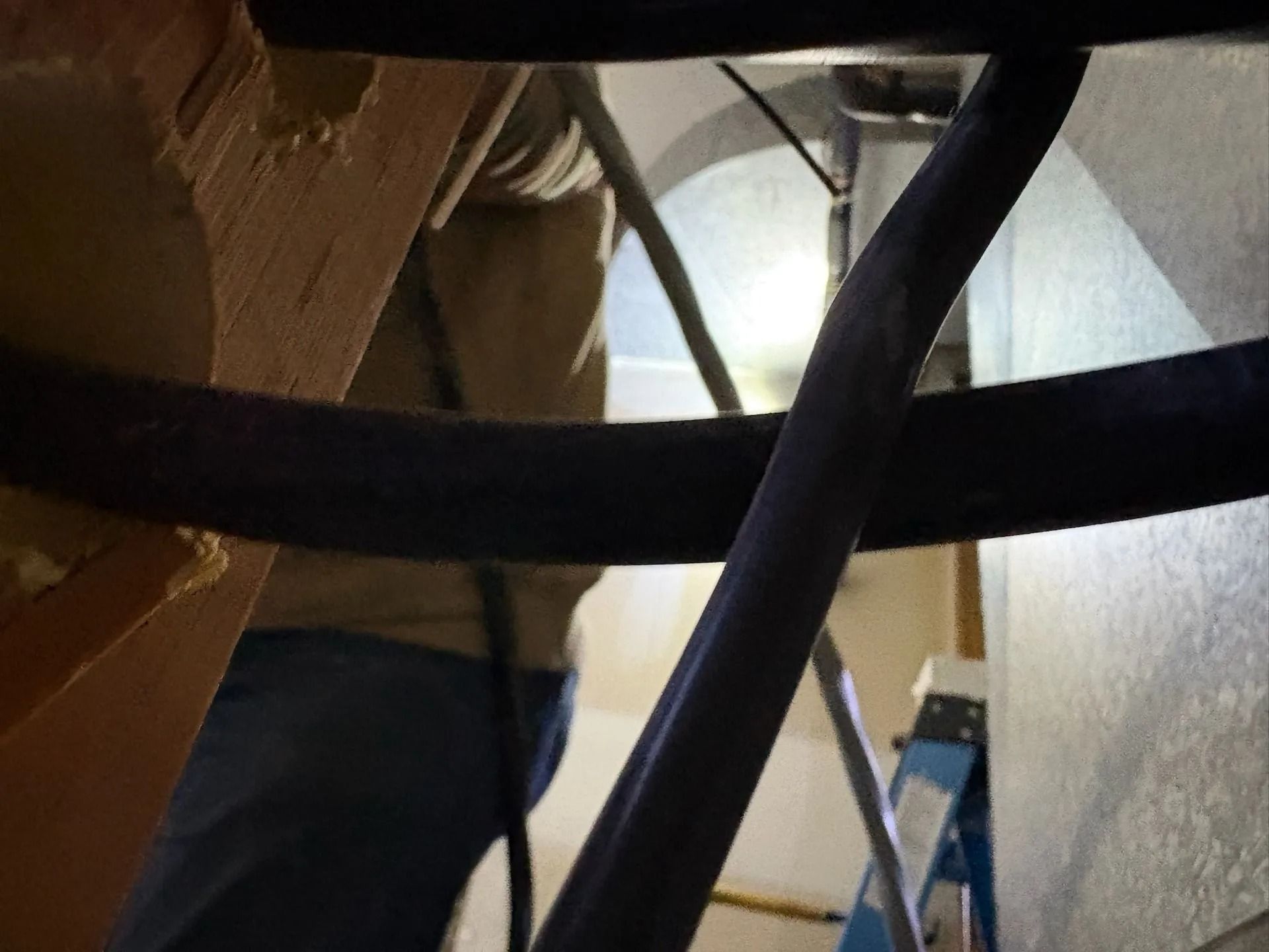 Person in jeans and a tan shirt working on ductwork, seen through pipes.