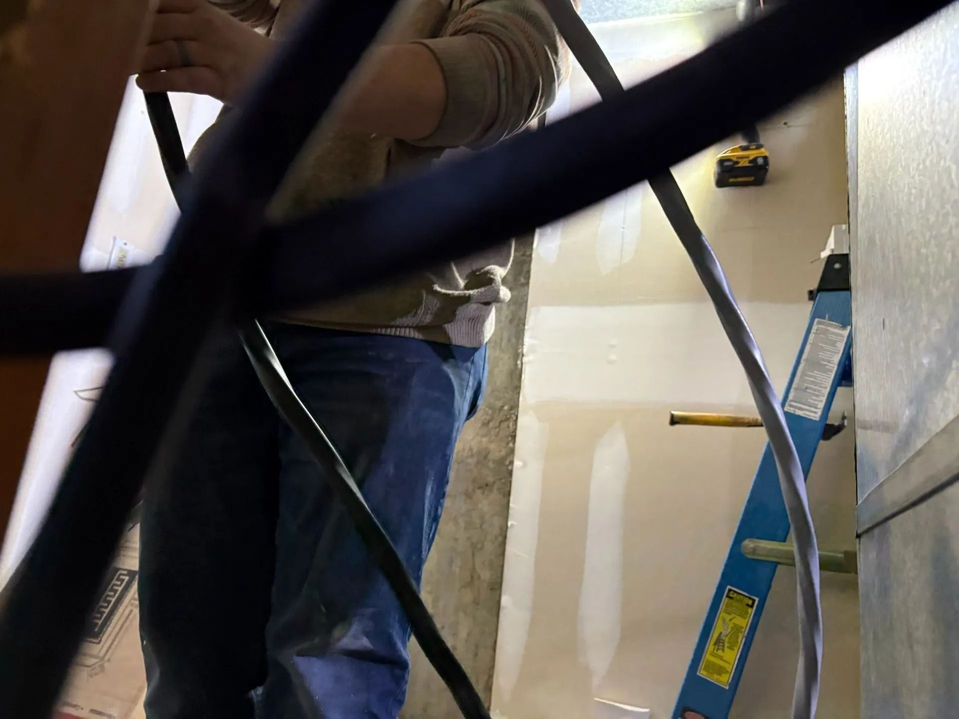 Person installing something near a ladder in a room, obscured by black pipes.