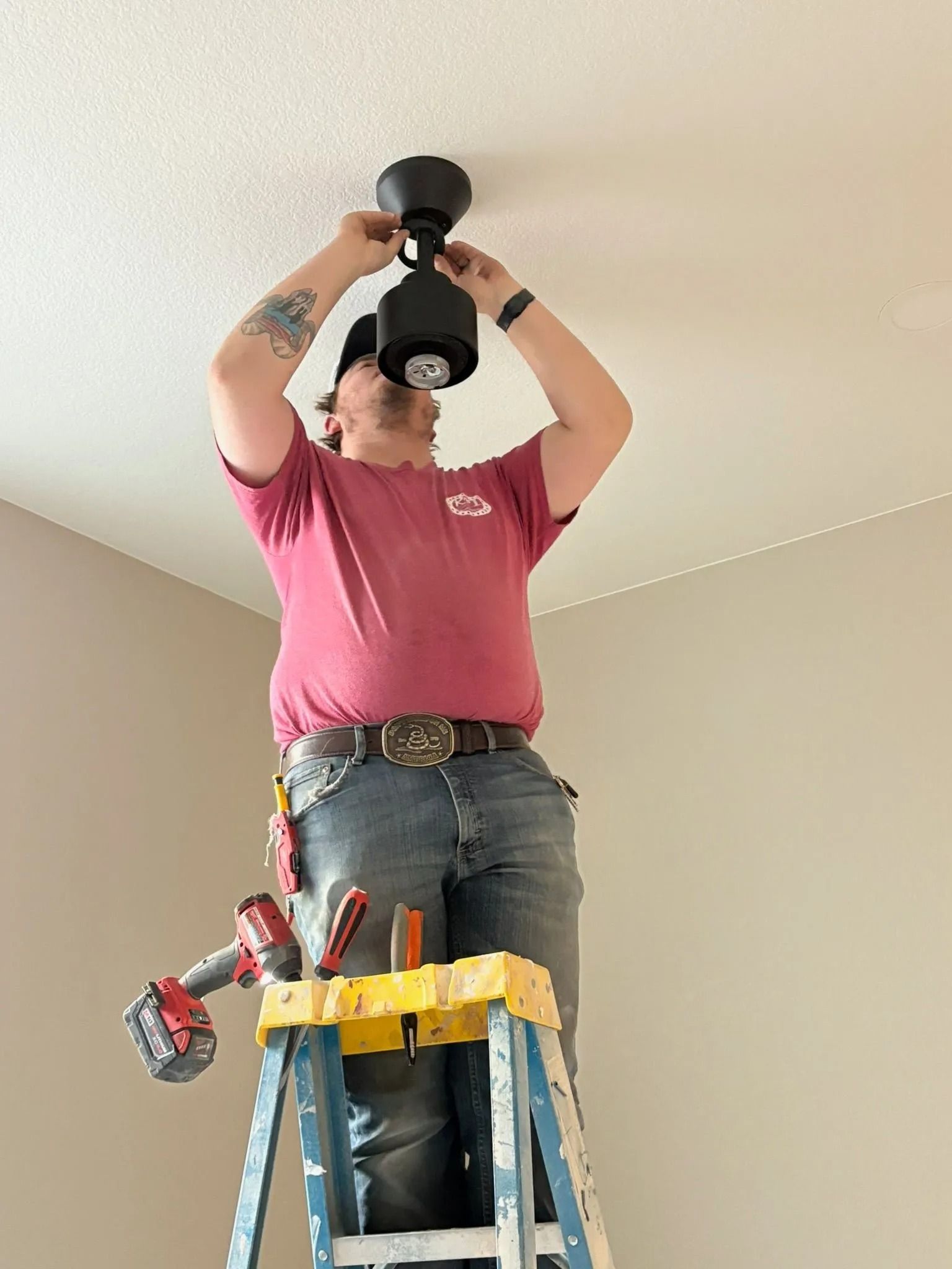Person on ladder installing a black ceiling light fixture in a room with light-colored walls and ceiling.
