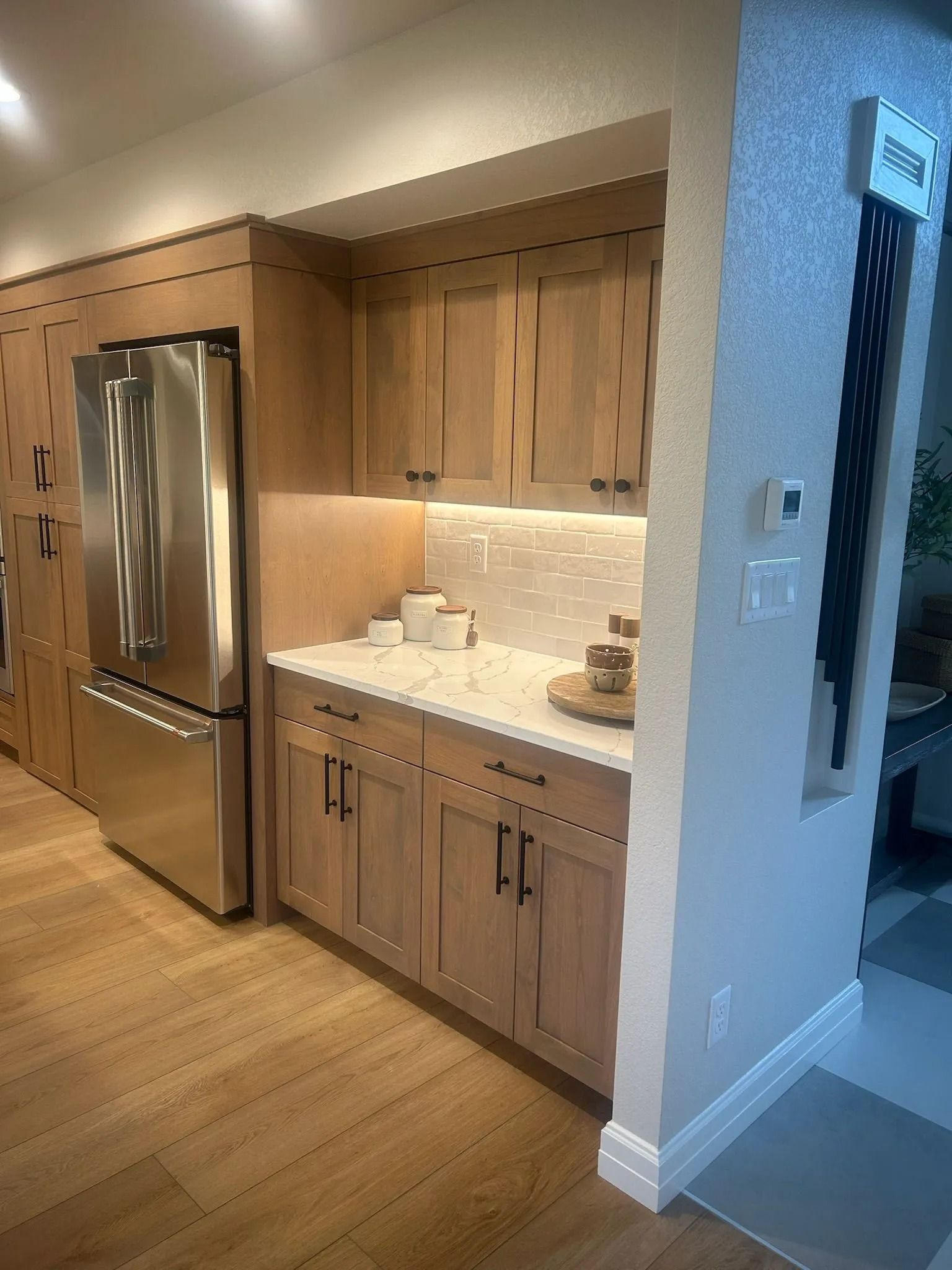 Kitchenette with light wood cabinets, stainless steel refrigerator, white countertops, and tiled backsplash.