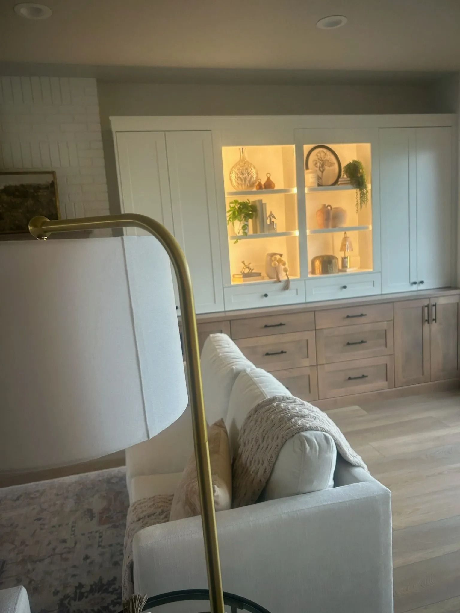 Living room with built-in cabinetry and a lit display. A white sofa sits in front of a brass lamp.