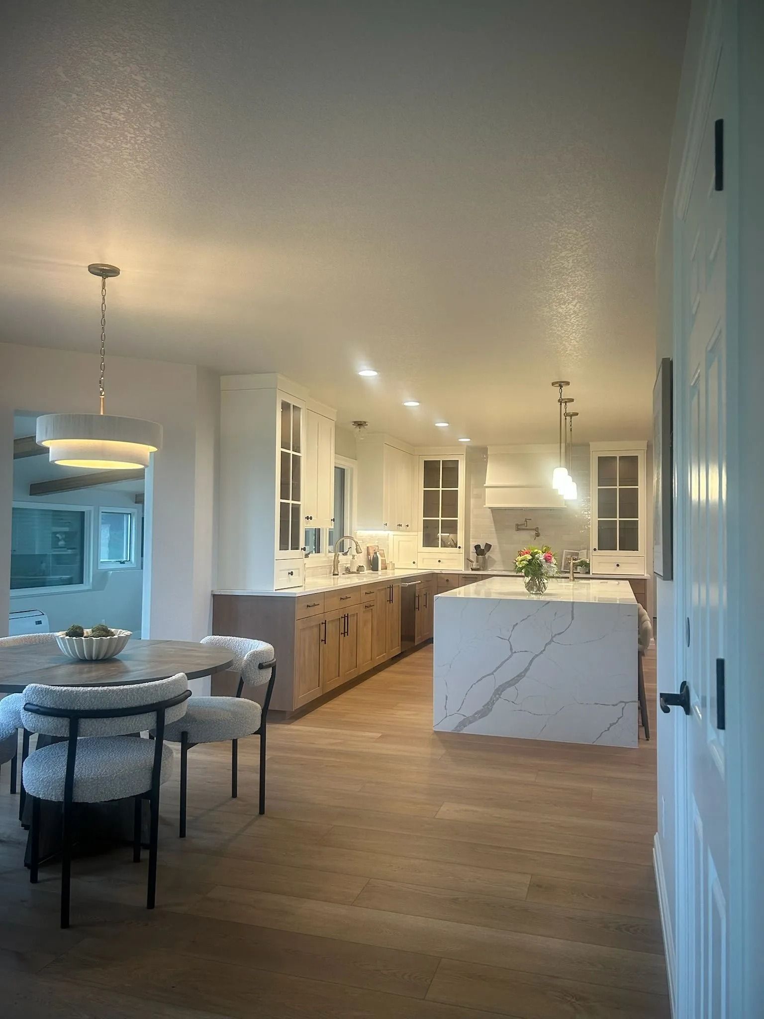 Modern kitchen with light wood cabinets, white countertops, and an island. Dining area visible.