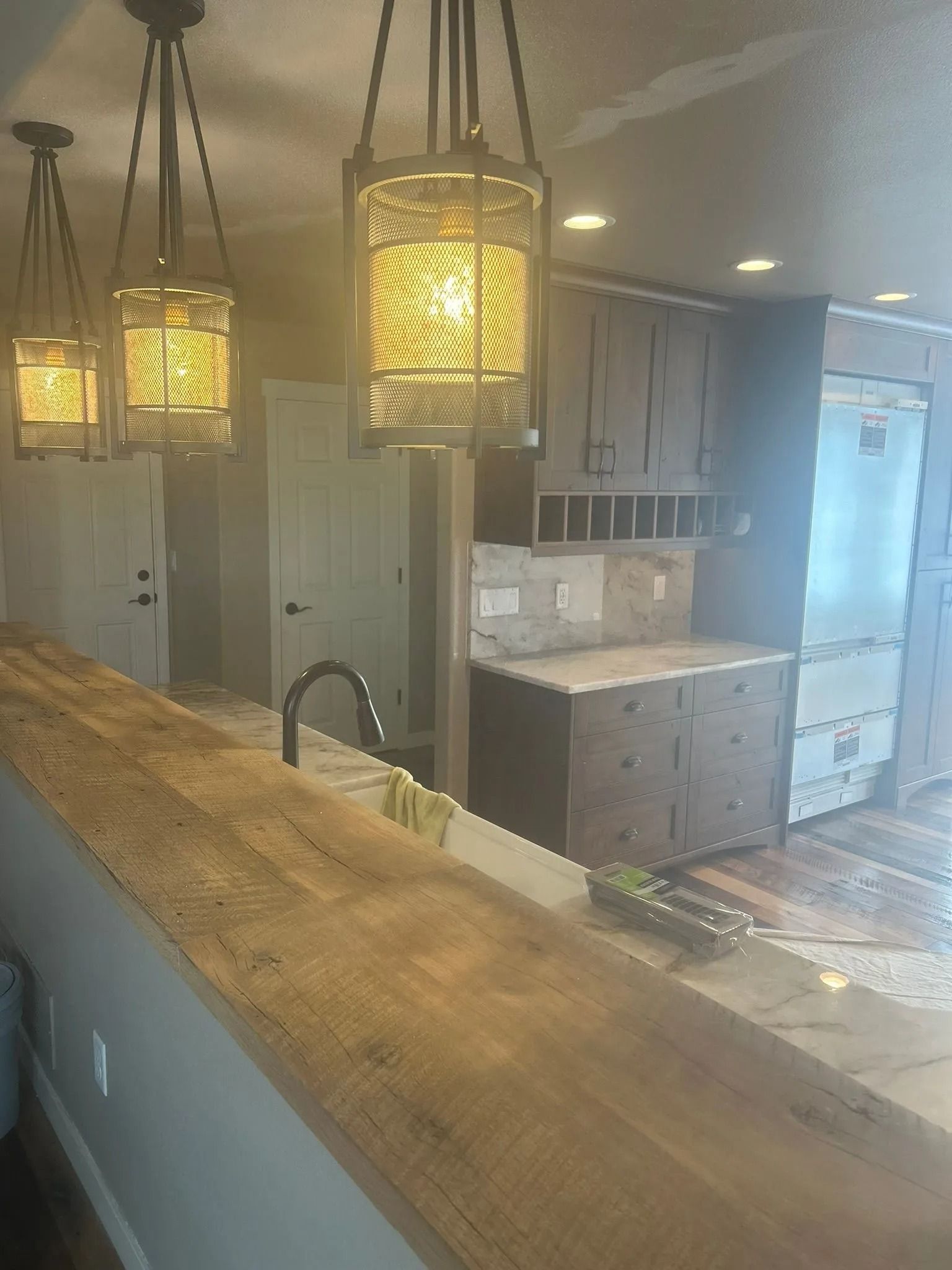Kitchen with wooden island, pendant lights, and dark cabinets.