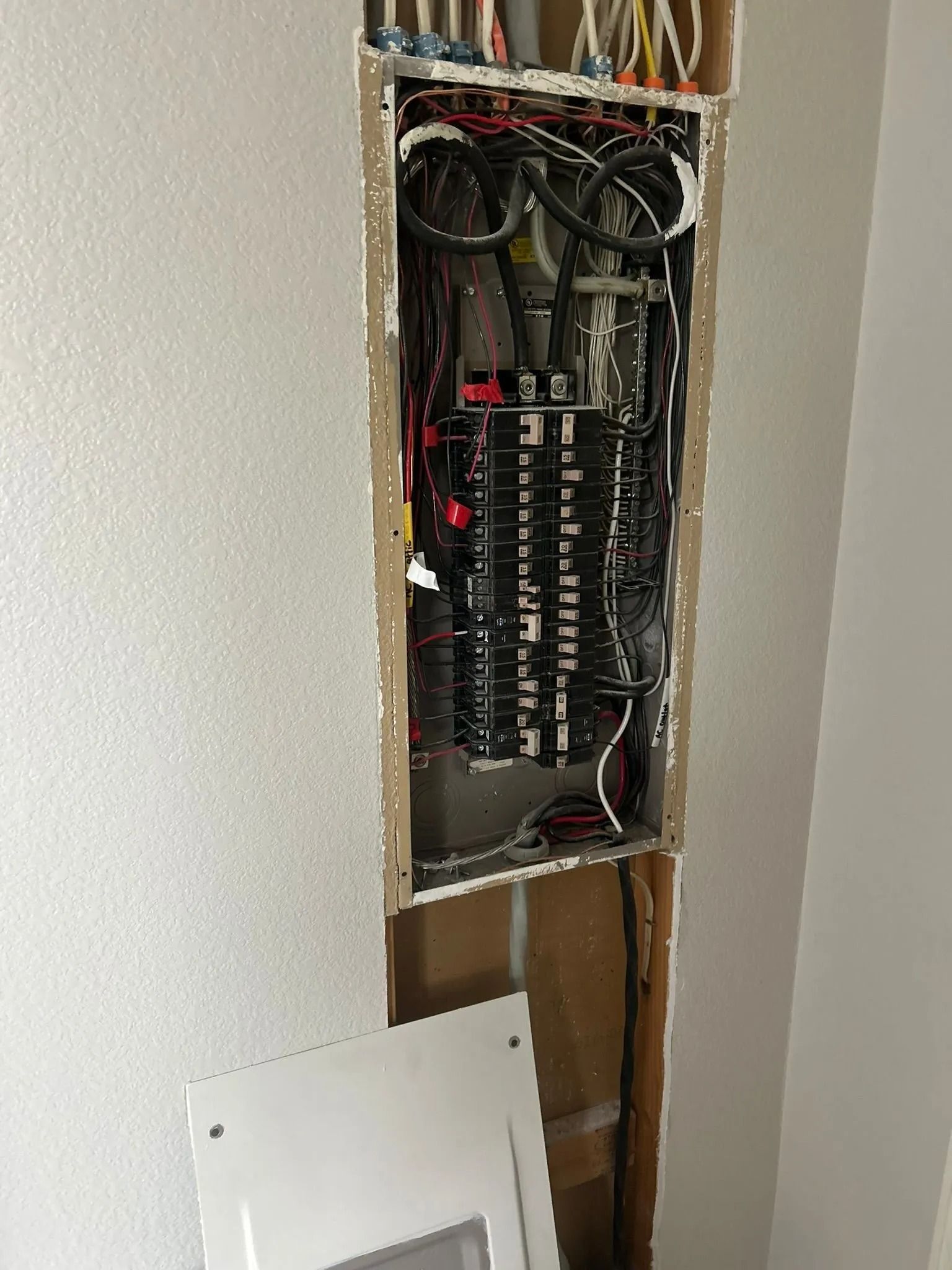 Electrical panel installed in a wall. Wiring is visible. The cover lies on the floor.