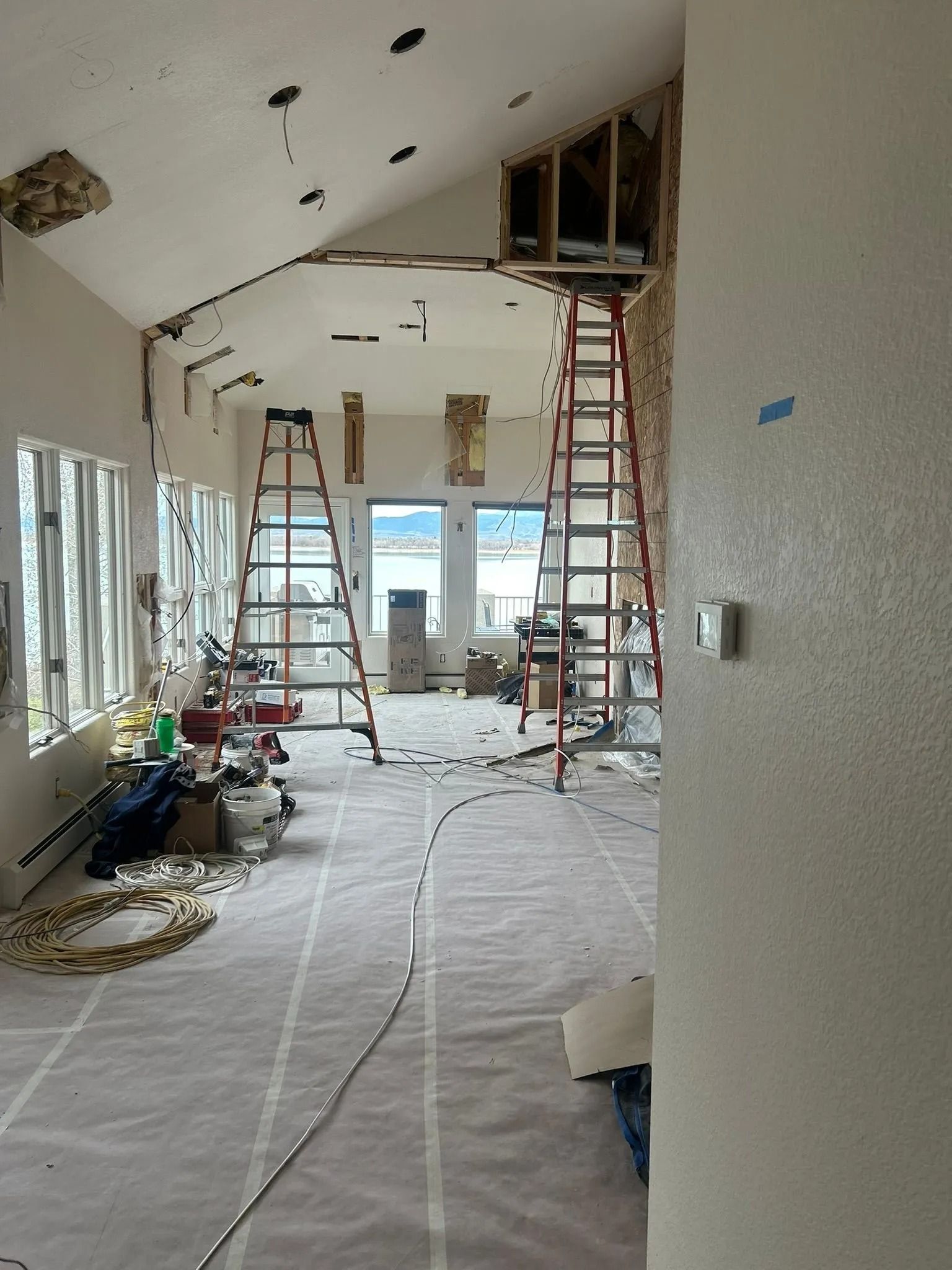 Interior construction in a room with two ladders, exposed wiring, and view through windows.