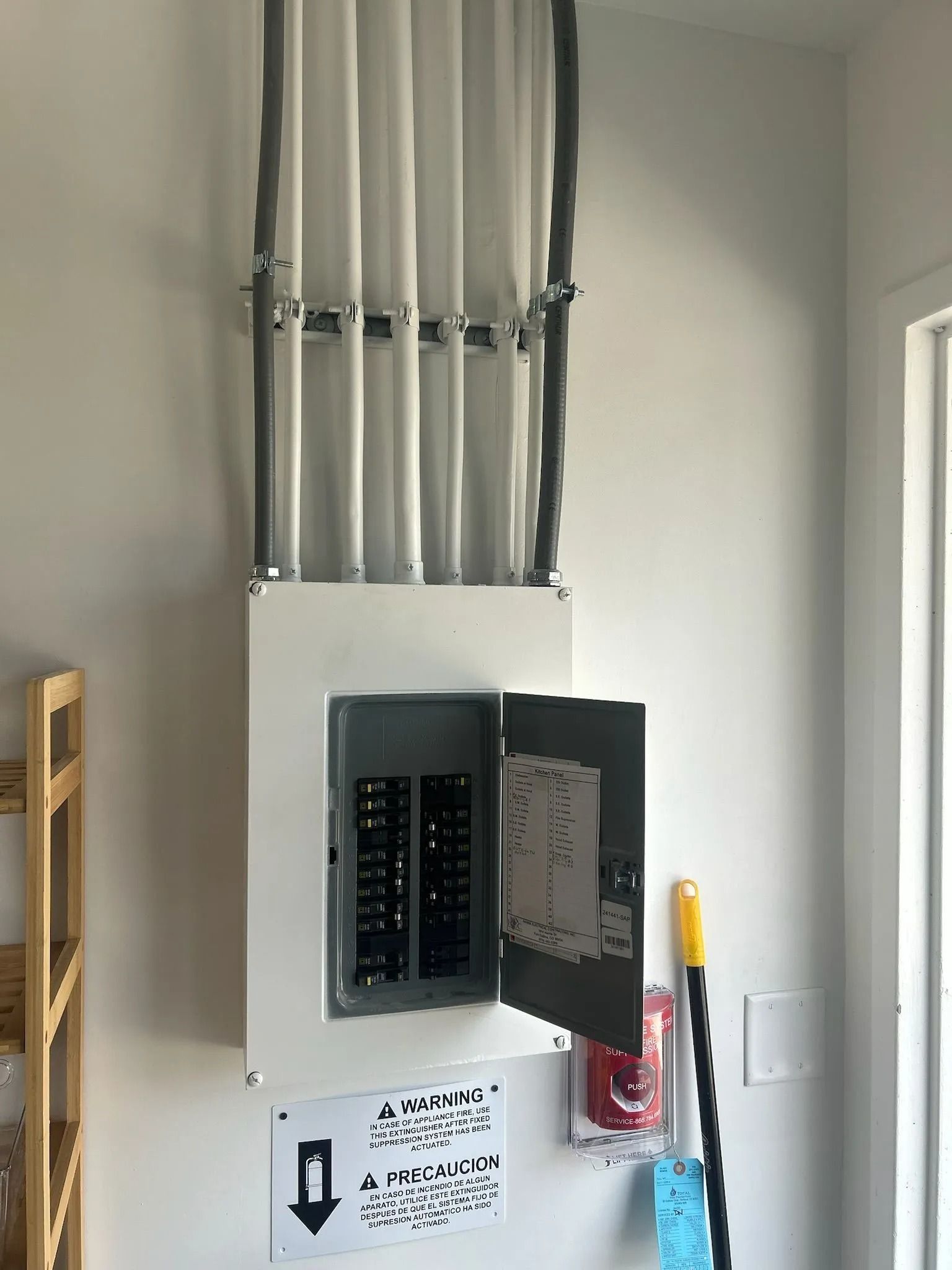 Electrical panel with open door, mounted on a white wall with conduit above.