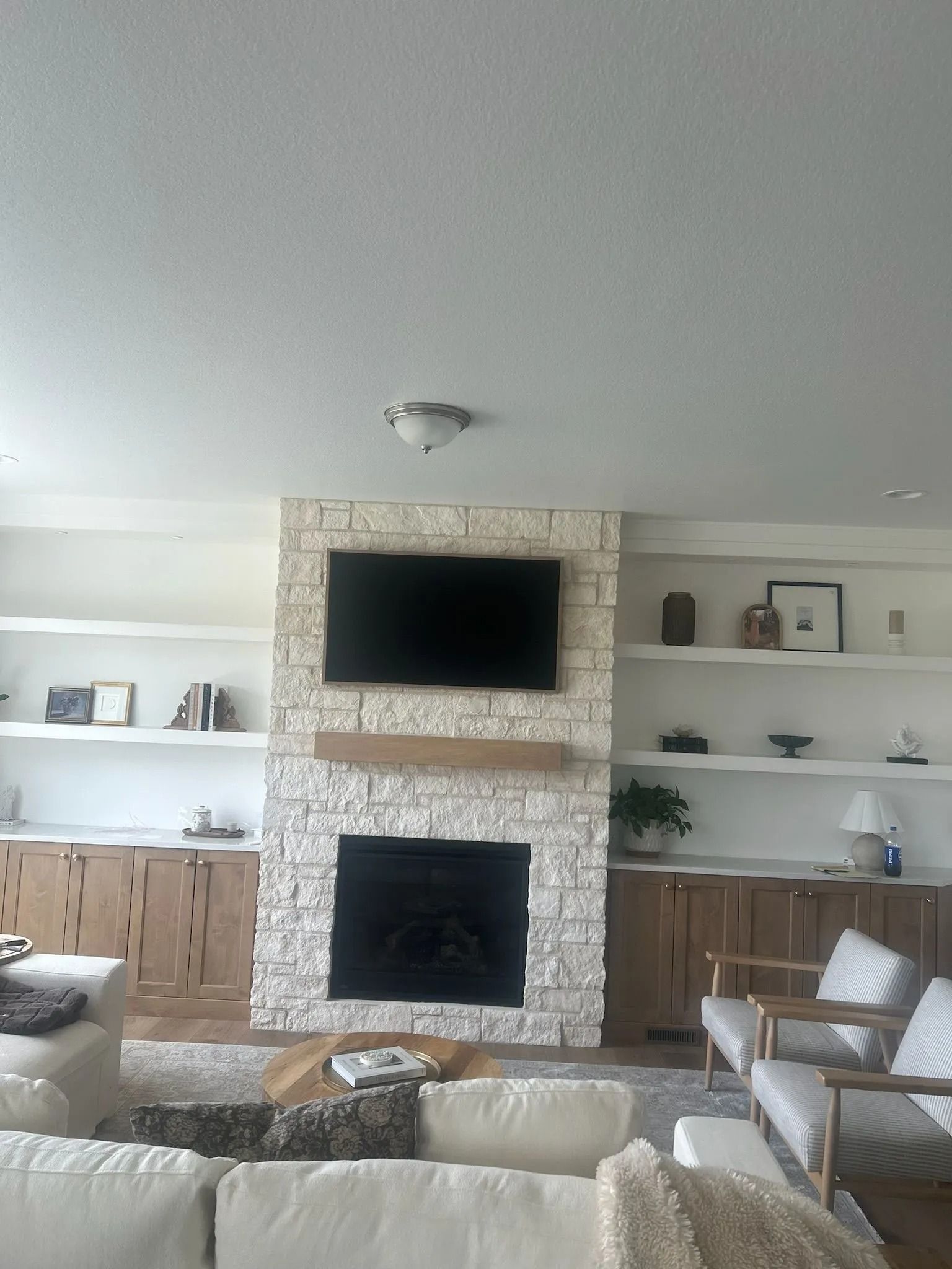 Living room with stone fireplace, TV, built-in shelves, and light-colored furniture.